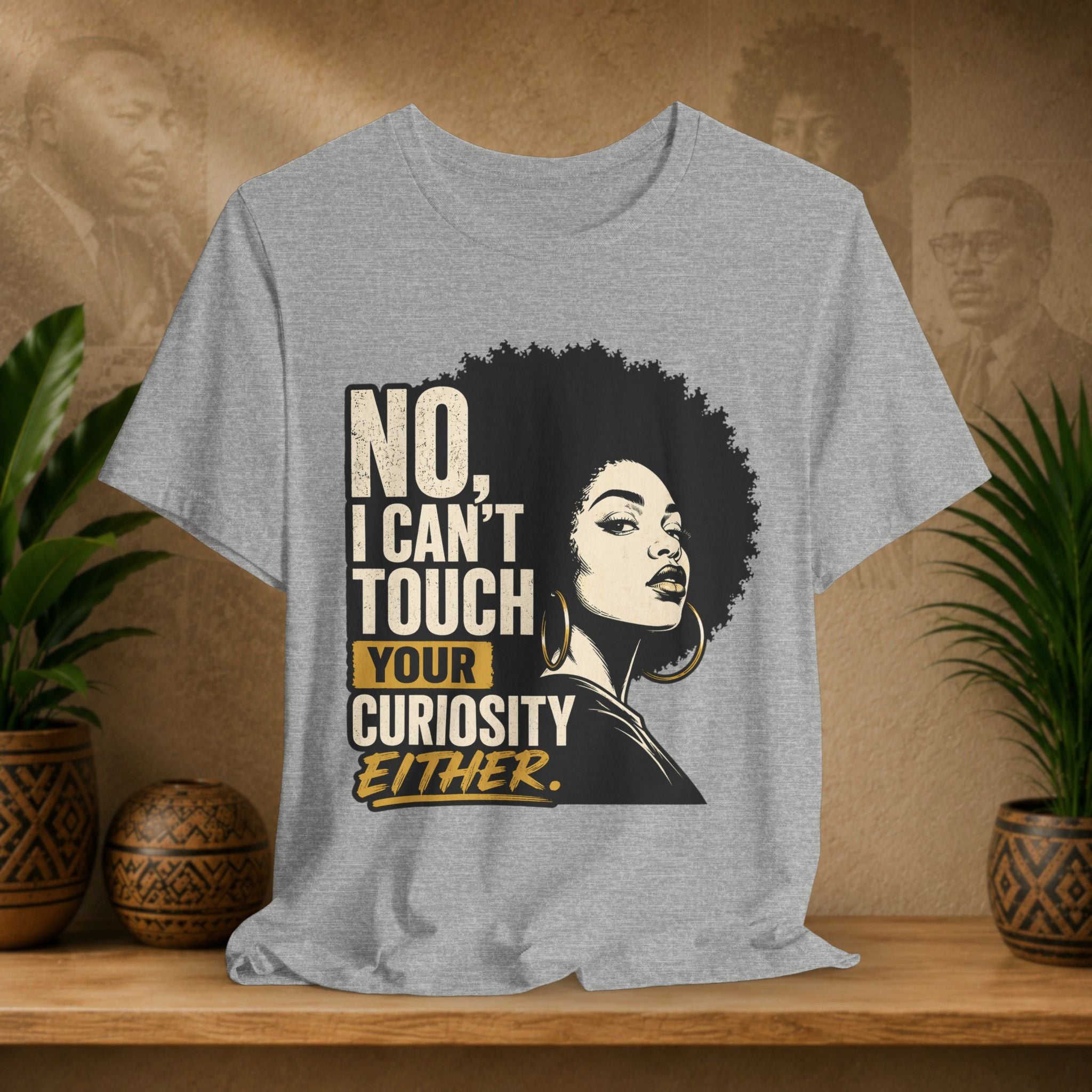 Gray t-shirt with a graphic of a woman with an afro and text on a wooden surface with plants and decorative items.