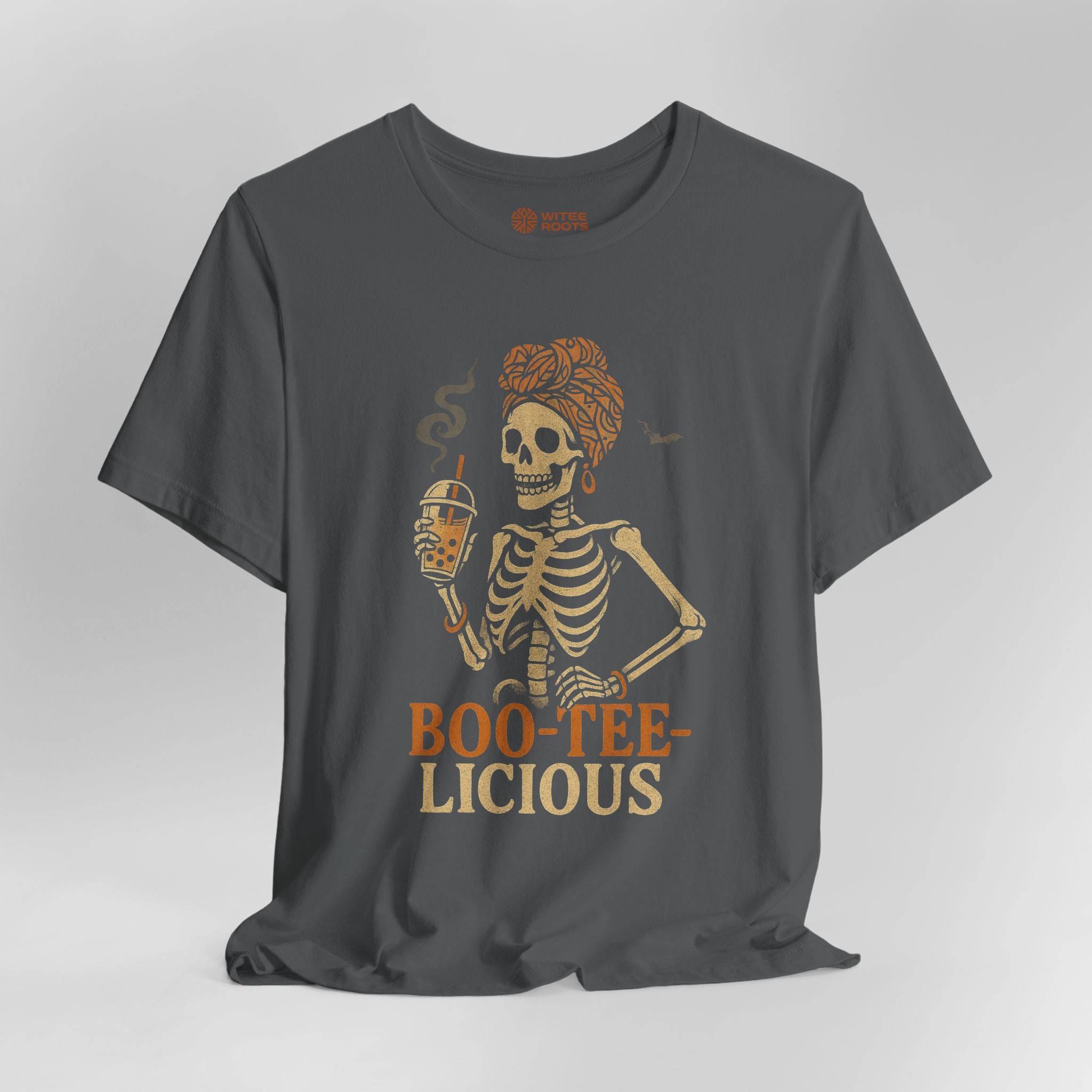 A dark gray crewneck t-shirt featuring a graphic of a skeleton woman with an orange turban holding a beer, with the text 'BOO-TEE-LICIOUS' printed below in orange and beige.