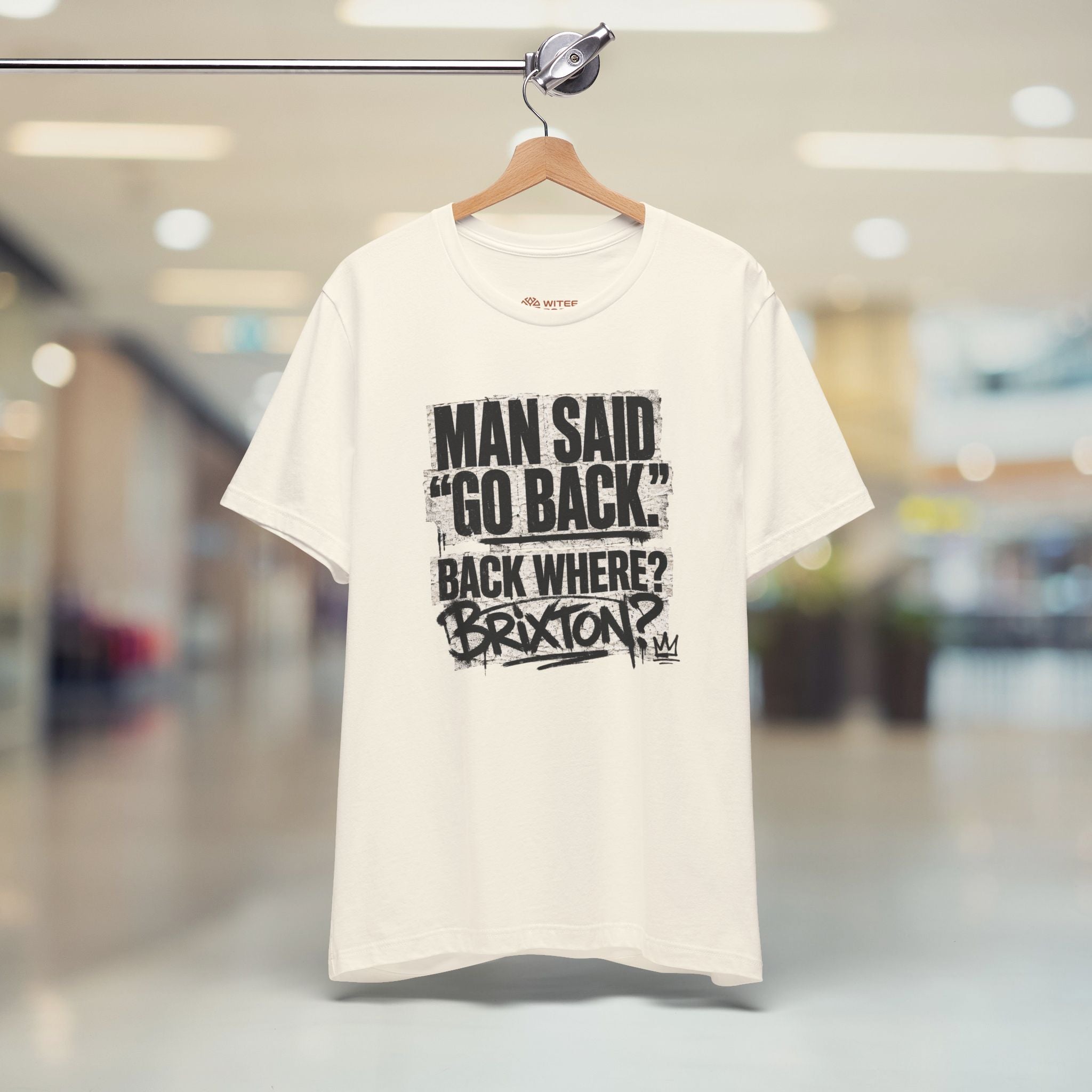 Beige t-shirt with black text on a hanger in a store setting