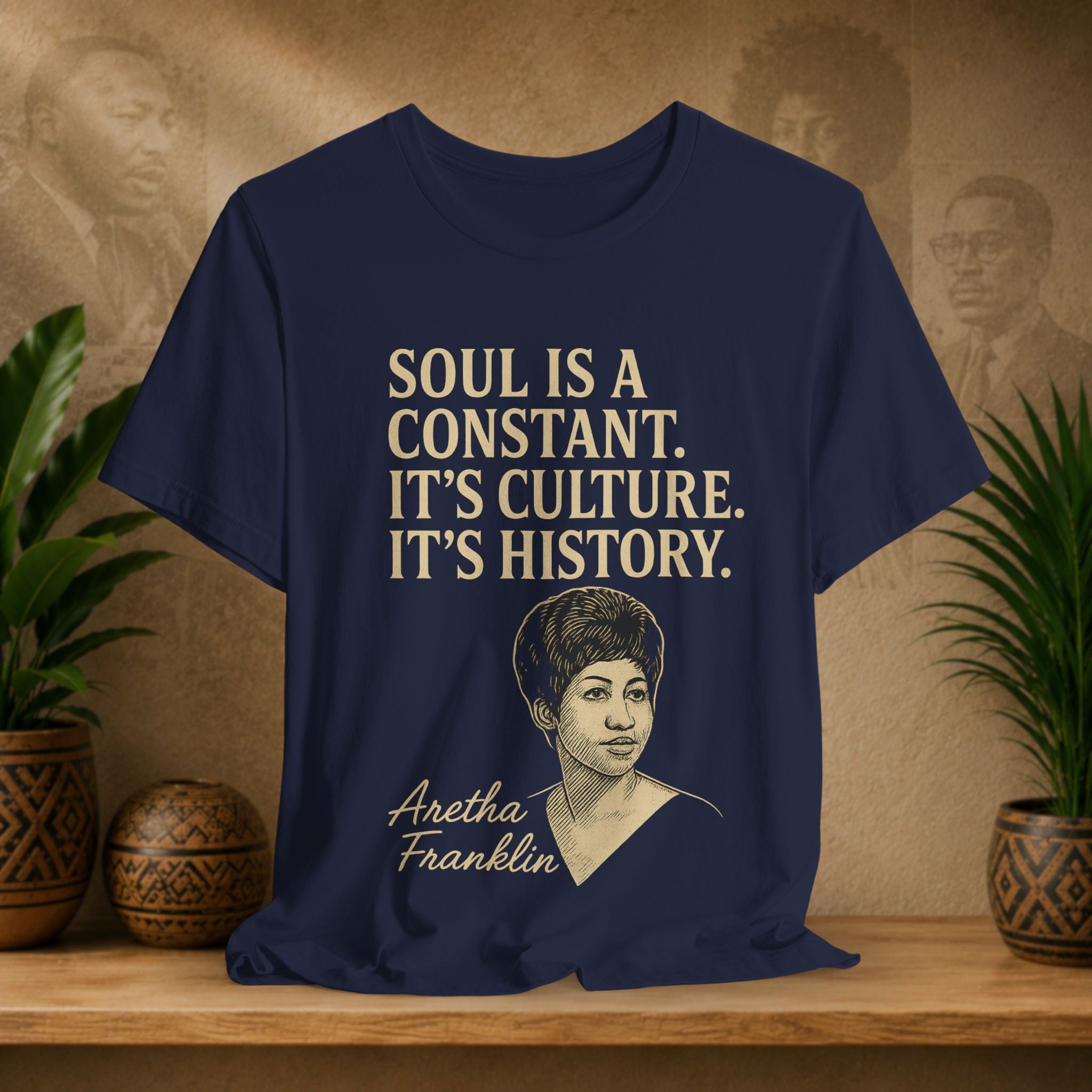 Navy blue t-shirt with Aretha Franklin quote on a wooden surface with plants and a vintage-style portrait in the background.