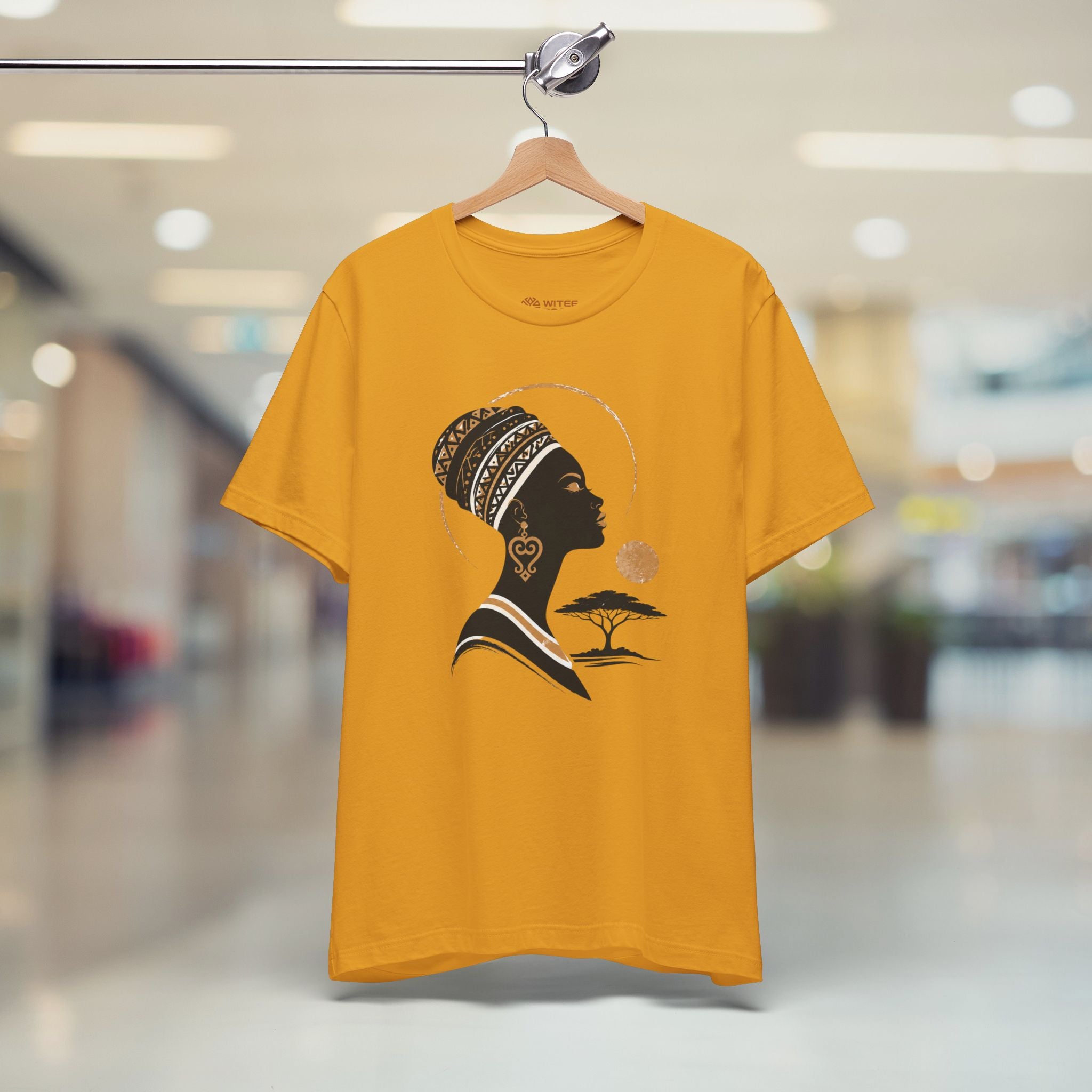 Yellow t-shirt with a graphic design of a silhouette of a woman with an afro, heart-shaped earrings, and a tree on a hanger.