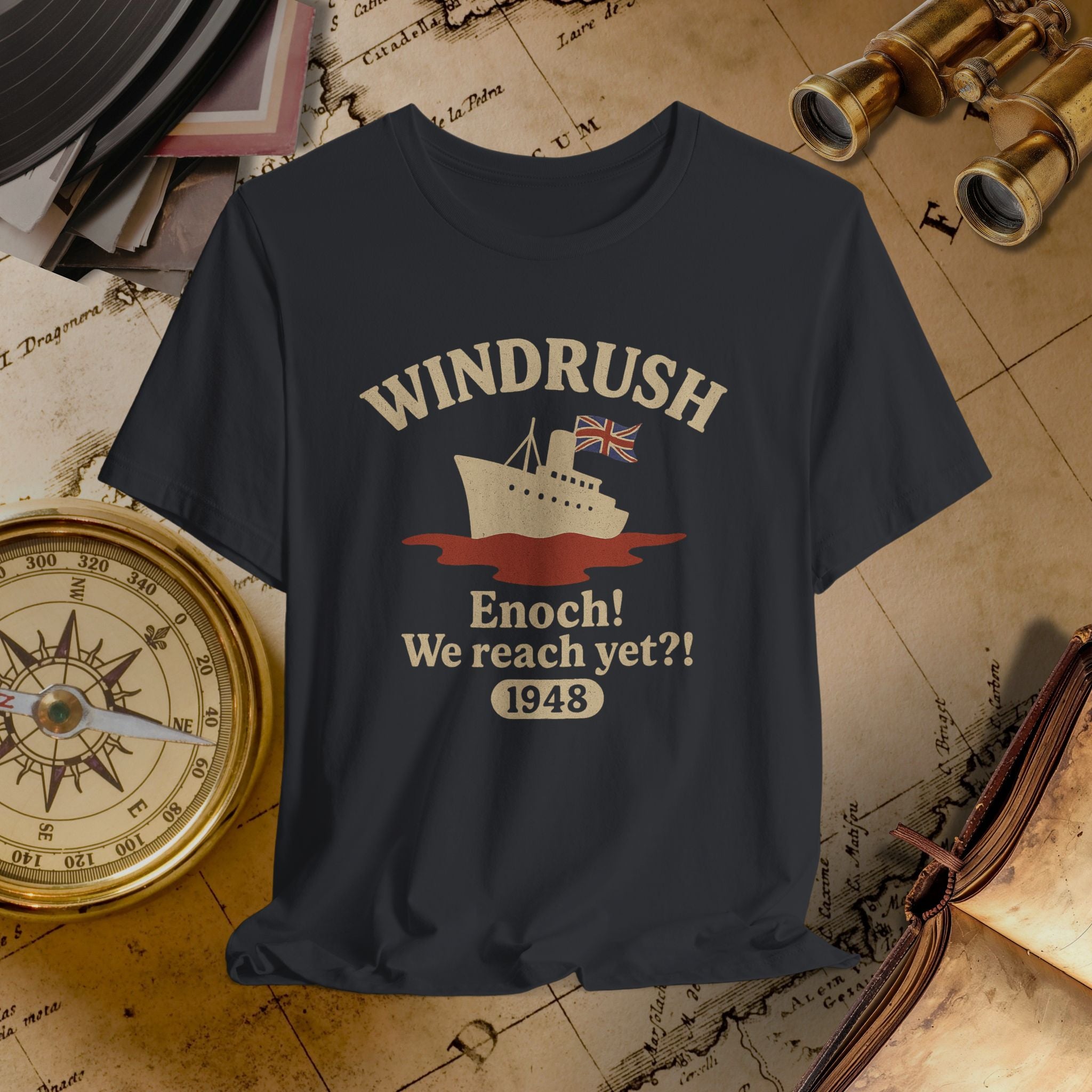 Black t-shirt with 'Windrush' design featuring a ship and text, placed on an old map background.