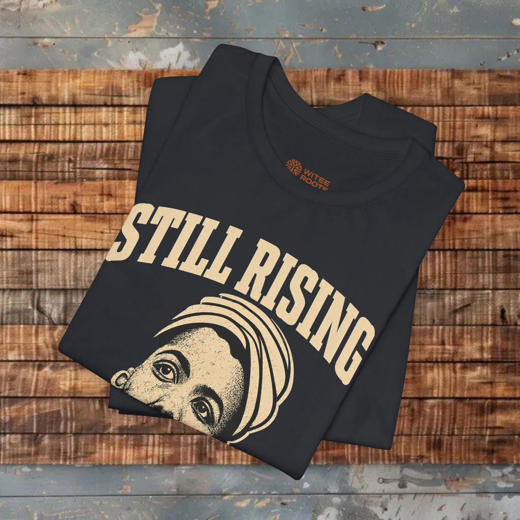 Black t-shirt with 'STILL RISING' text and graphic on a wooden surface