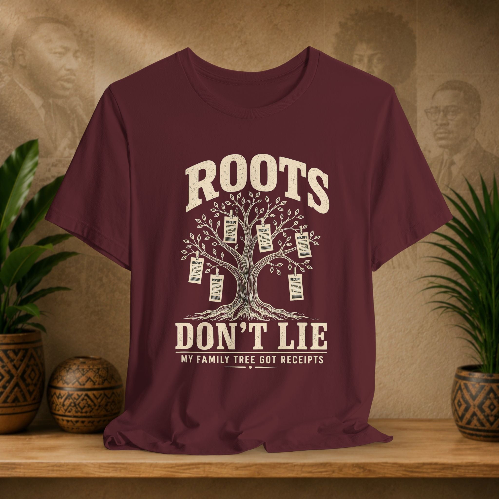 Maroon t-shirt with family tree graphic and text on a wooden surface with plants and decorative items.