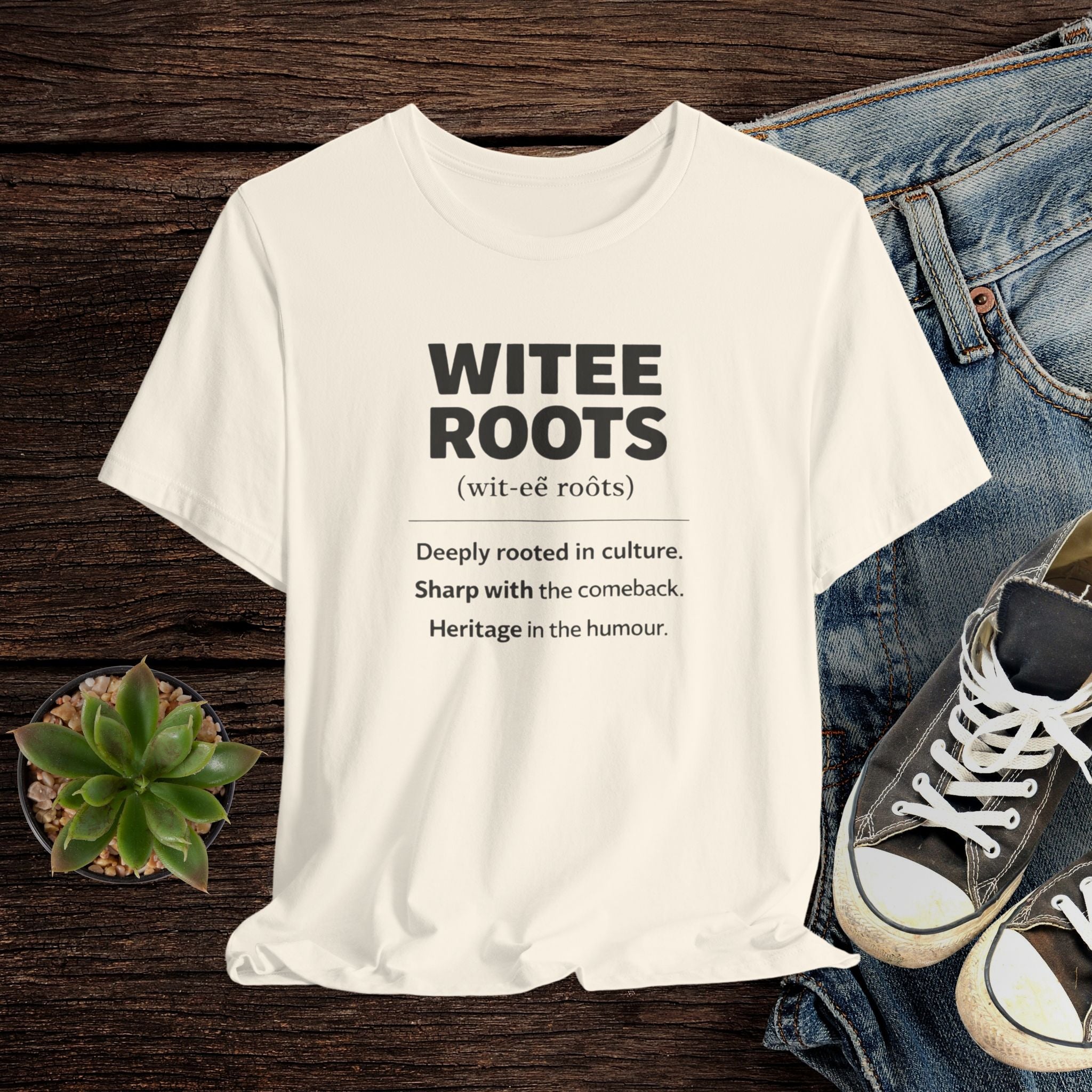 Beige t-shirt with 'WITEE ROOTS' text design on a wooden surface with jeans and sneakers.
