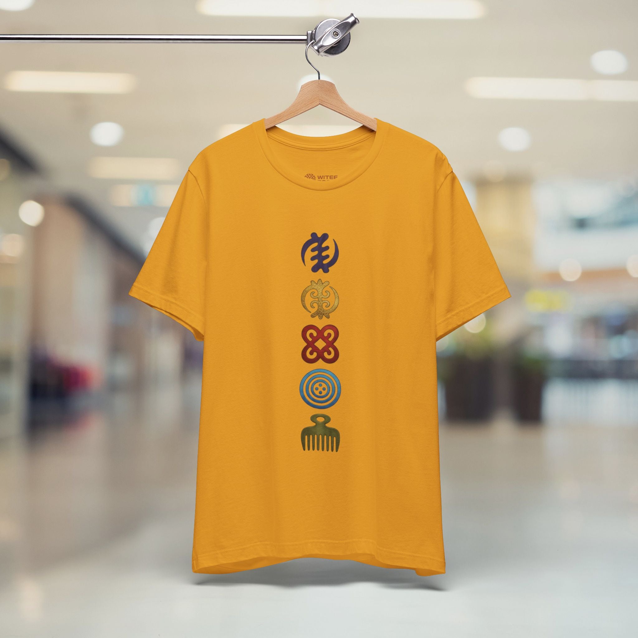 Mustard t-shirt with colorful symbols on a hanger in a store.