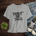 Gray t-shirt with 'PROTECT THE DOLLS' text, paired with jeans and sneakers on a wooden surface.