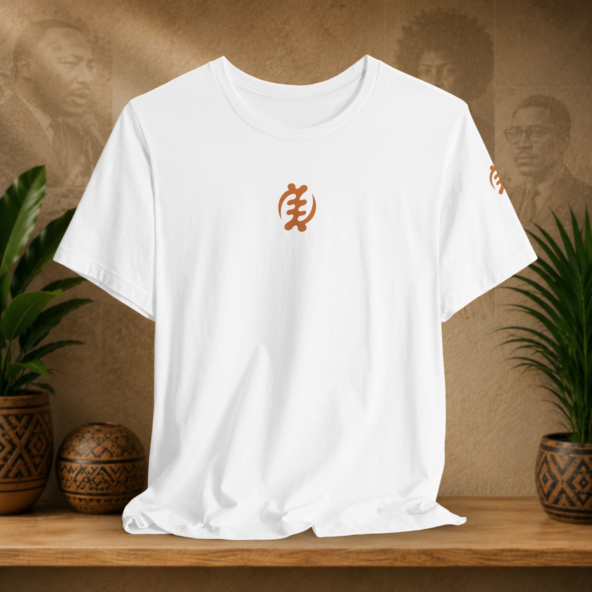 White t-shirt with orange logo on a wooden shelf with plants and decorative items.