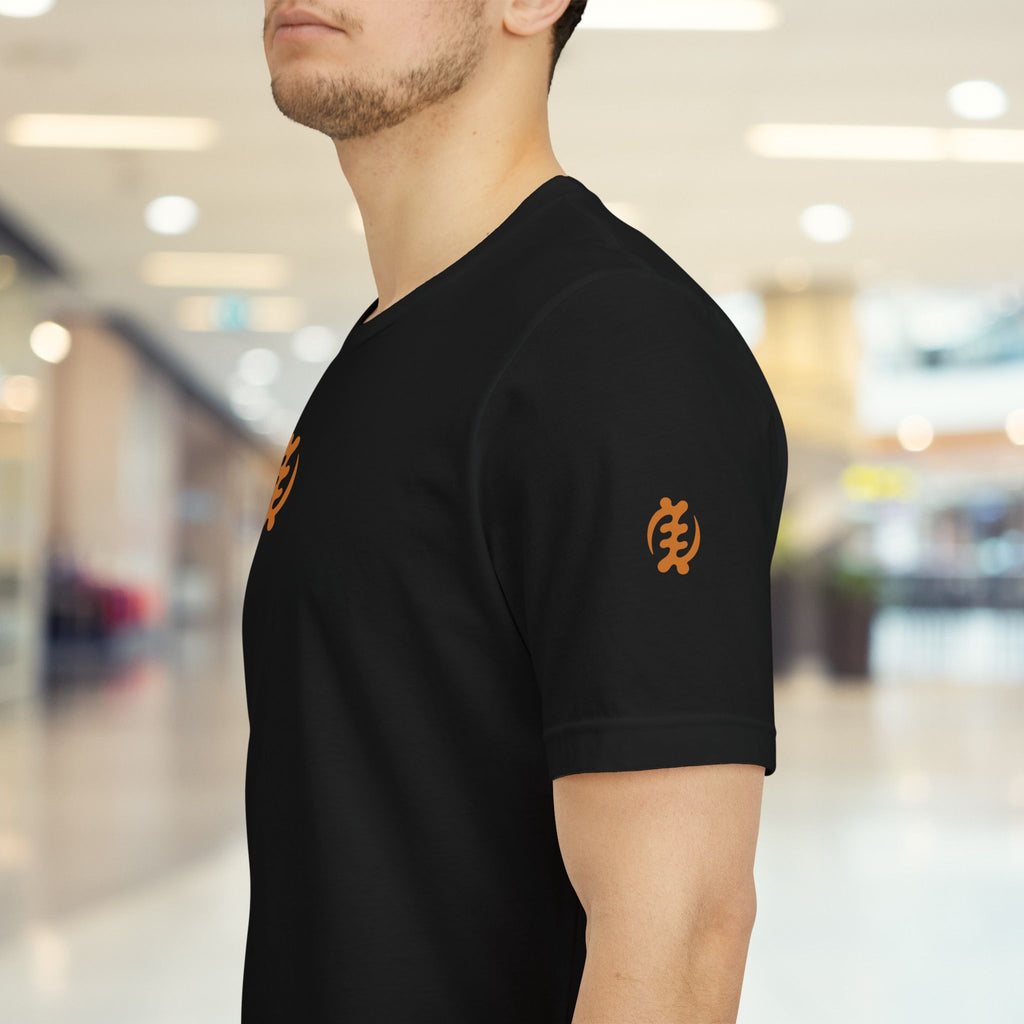 Person wearing a black t-shirt with orange logos in a blurred indoor setting