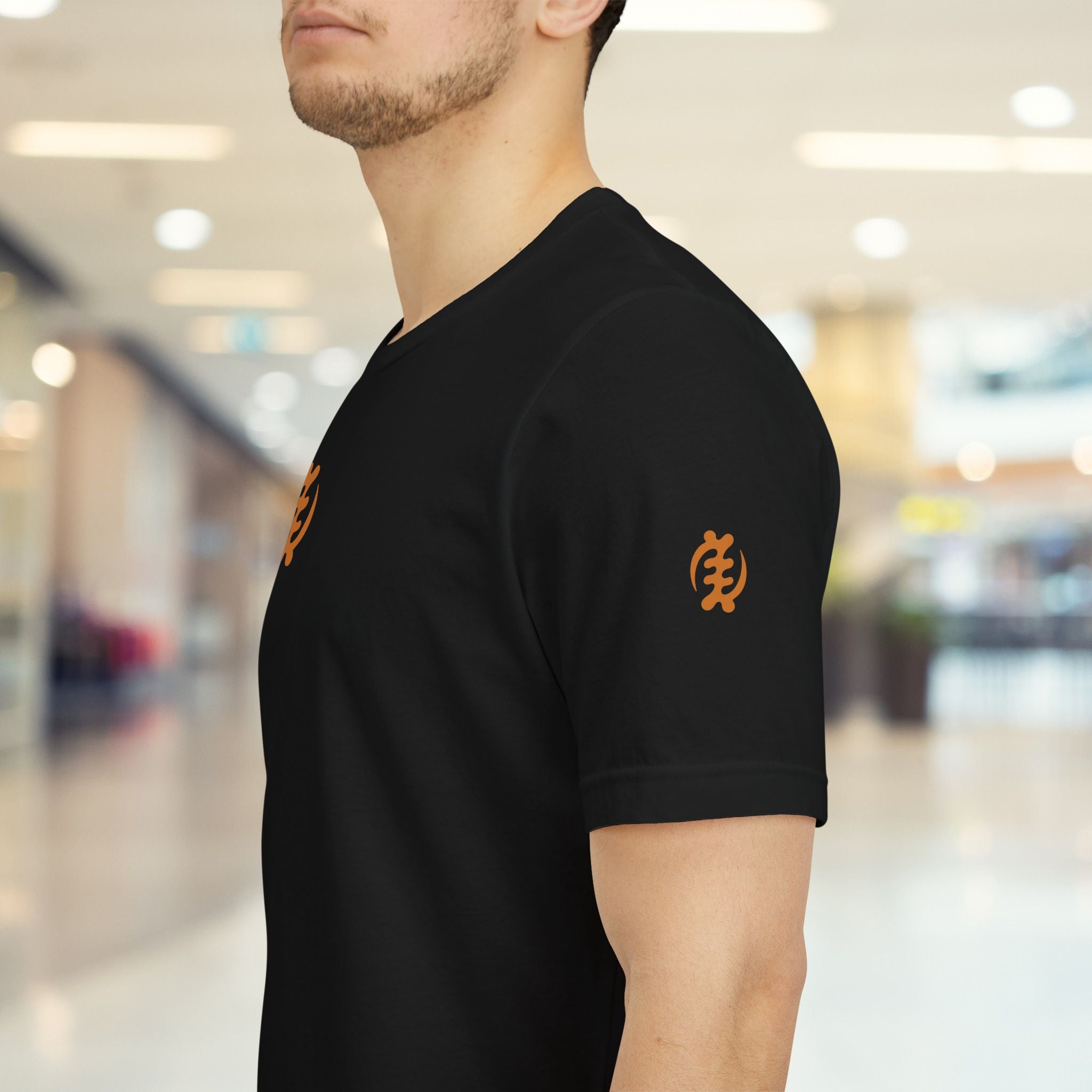 Person wearing a black t-shirt with orange logos in a blurred indoor setting