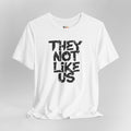 White t-shirt with black text 'THEY NOT LIKE US' on a gray background