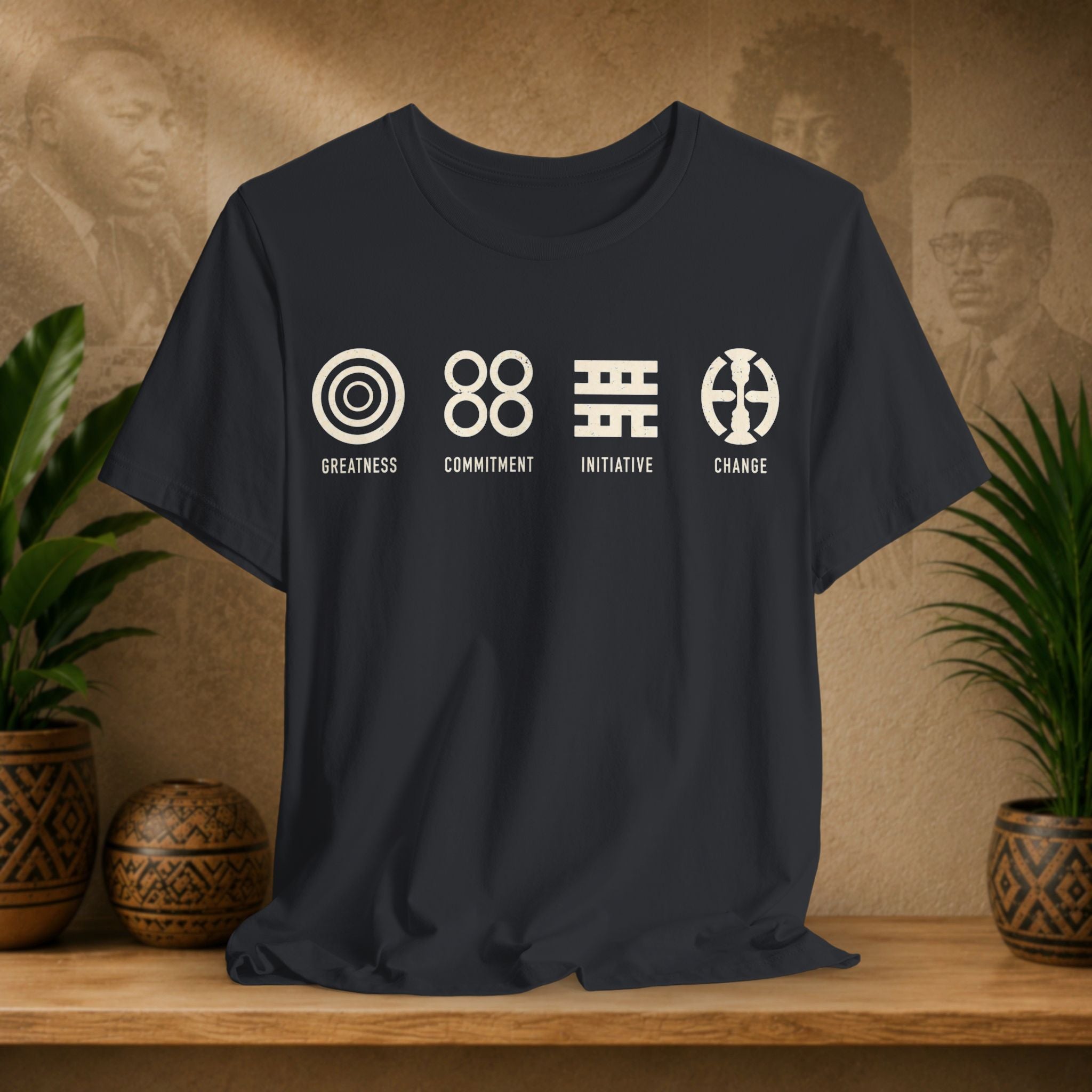 Black t-shirt with white graphics and text on a wooden surface with plants and a textured wall background