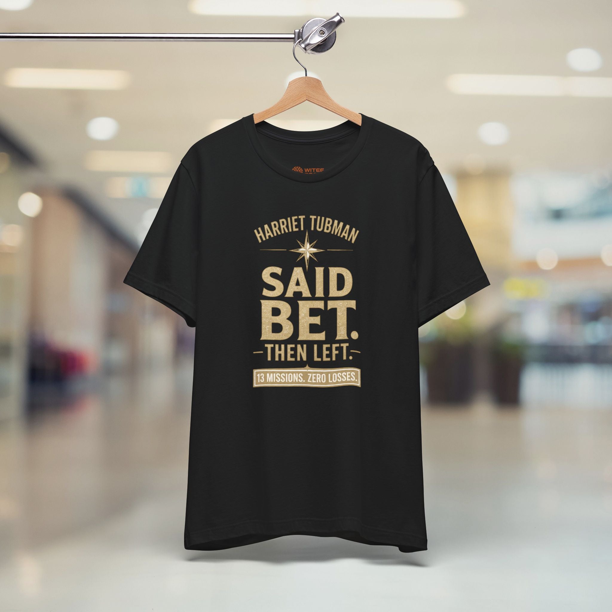 Black t-shirt with gold text on a hanger in a store setting