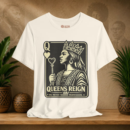 Beige t-shirt with 'Queens Reign' graphic design on a wooden surface with plants and a textured wall background.