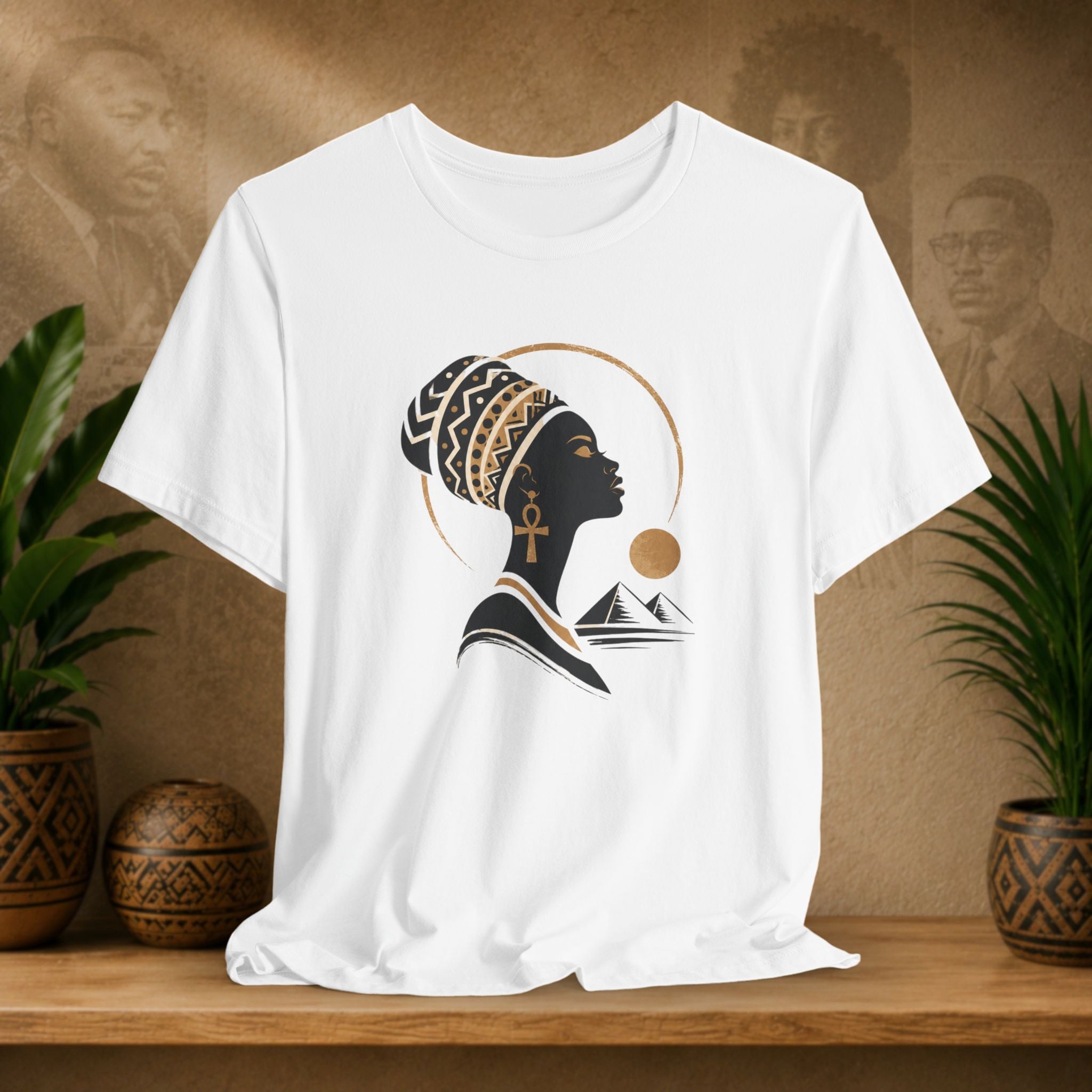 White t-shirt with a black silhouette design of a woman with an ankh and mountains on a wooden shelf.