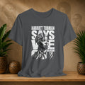 Gray t-shirt with Harriet Tubman graphic and text on a wooden surface with plants and decorative items.