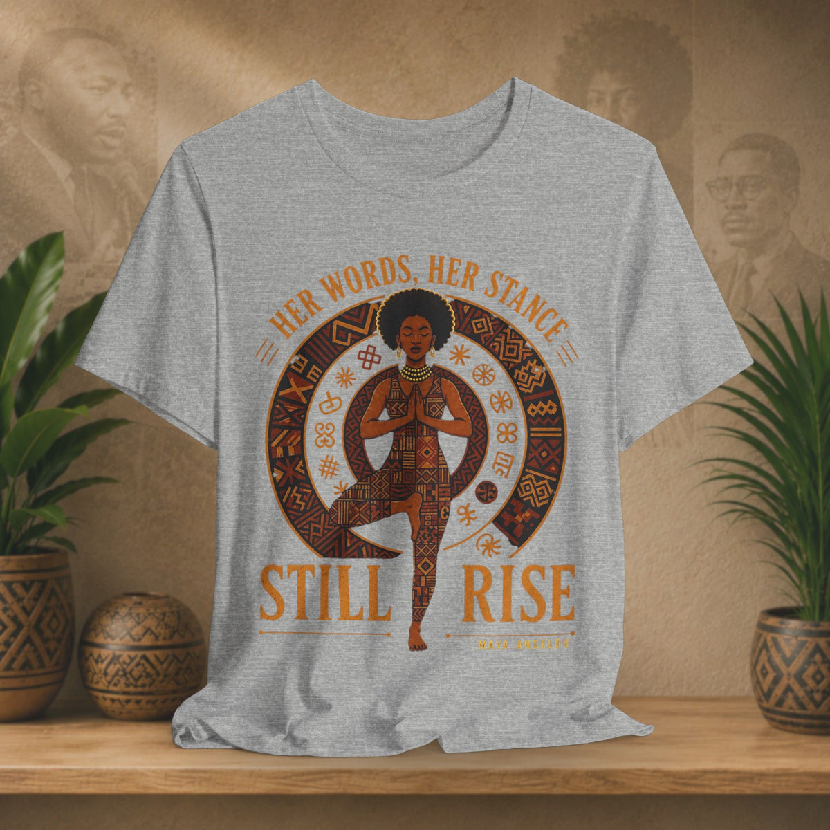 A heather gray graphic t-shirt displayed on a wooden shelf. The shirt features a circular graphic of a woman in a yoga pose surrounded by patterns, with the text 'HER WORDS.