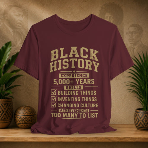 Maroon t-shirt with 'Black History' text on a wooden shelf with decorative items.