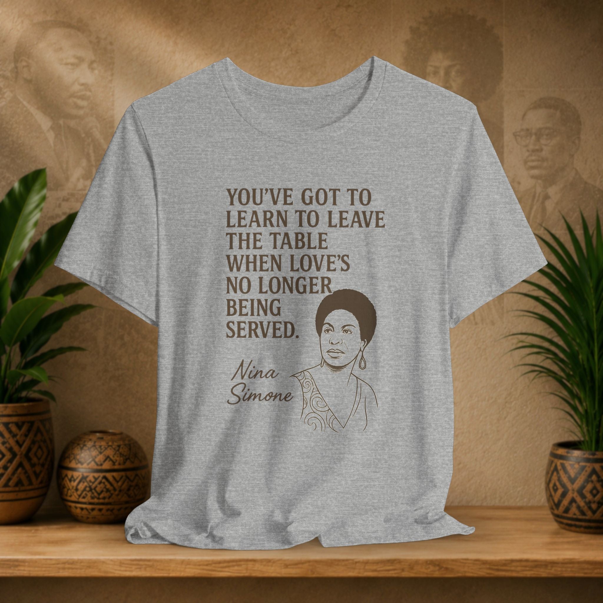 Gray t-shirt with Nina Simone quote and portrait on a wooden shelf with plants and decorative items.