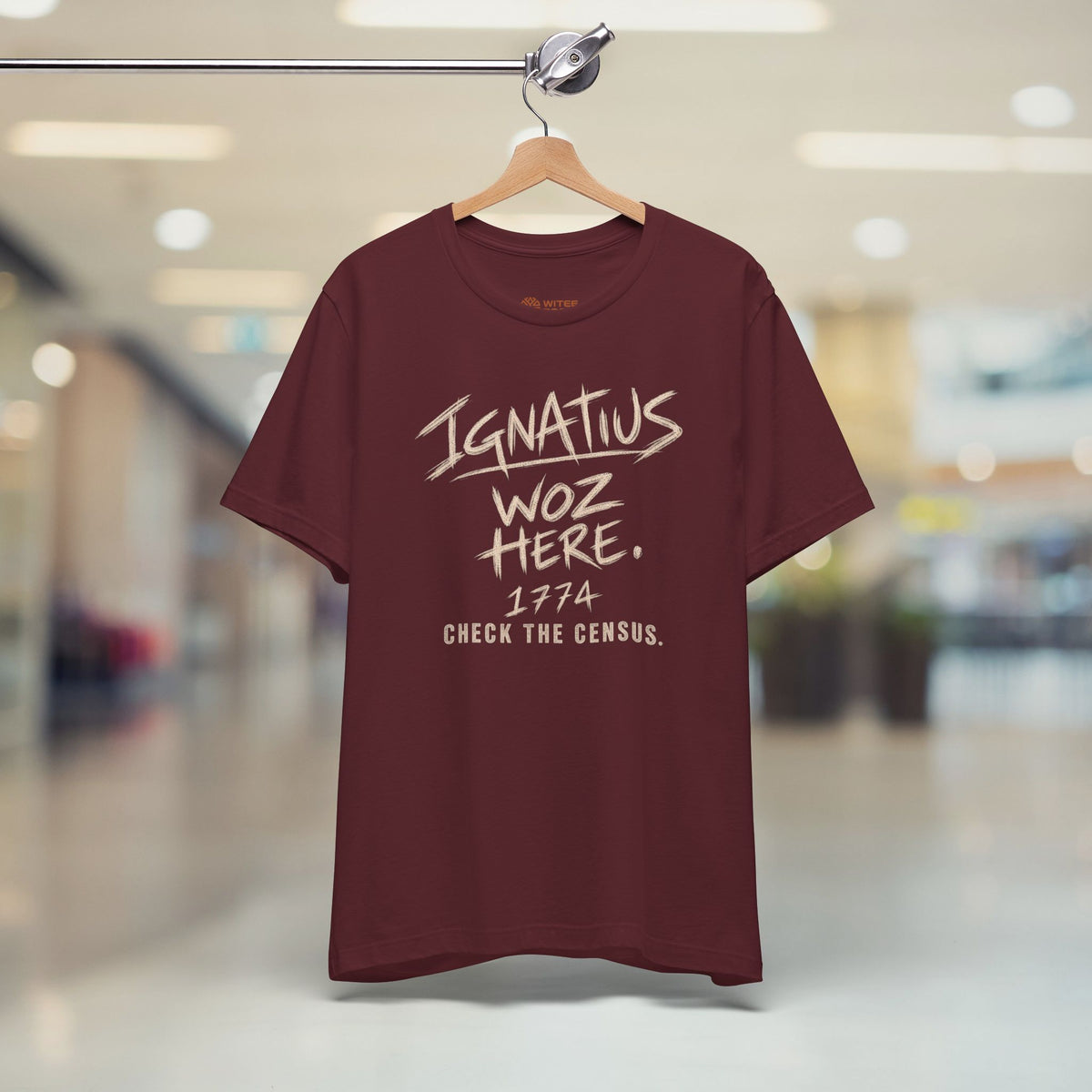 Maroon t-shirt with text on a hanger in a store setting