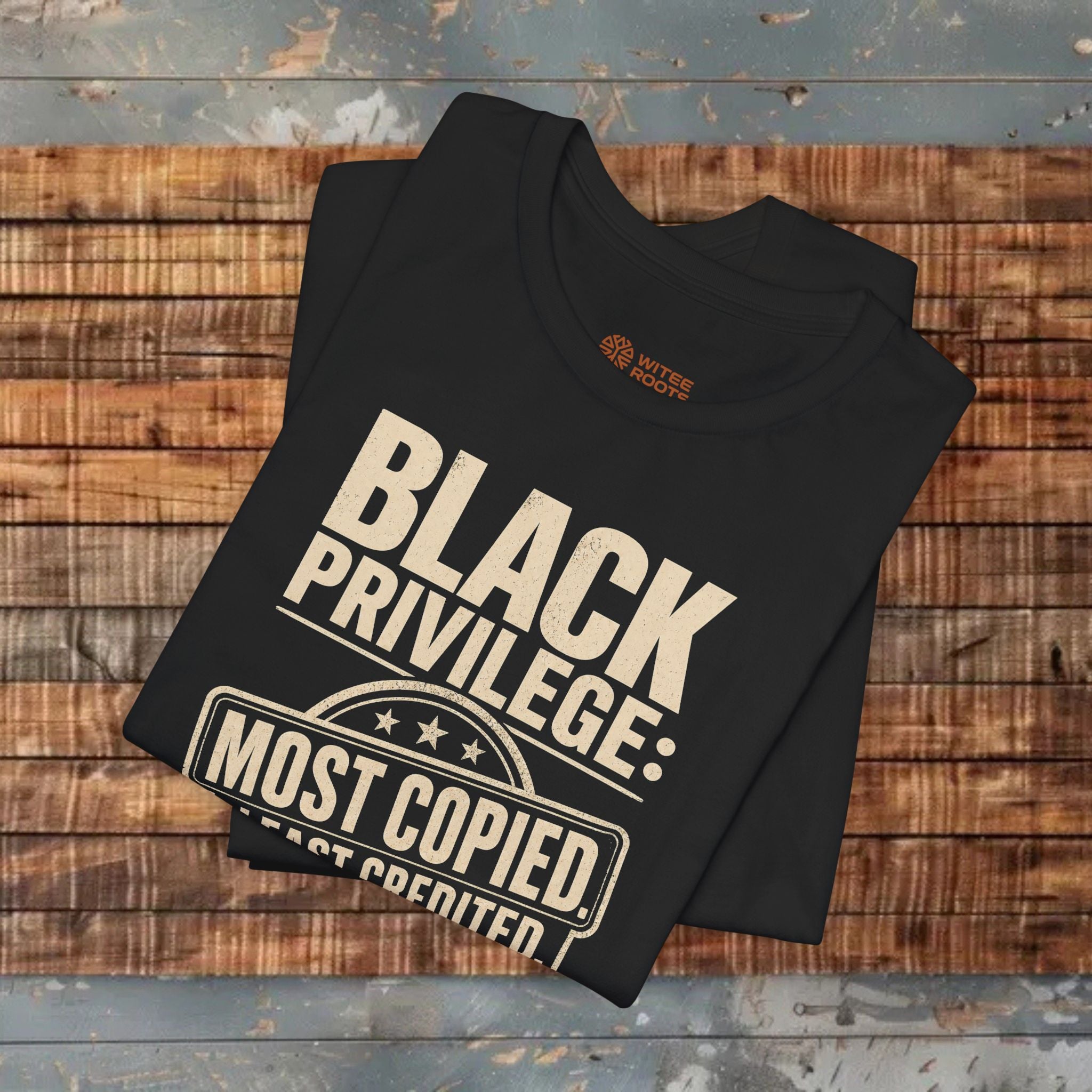 Black t-shirt with 'Black Privilege: Most Copied, Least Credit' text on a wooden surface