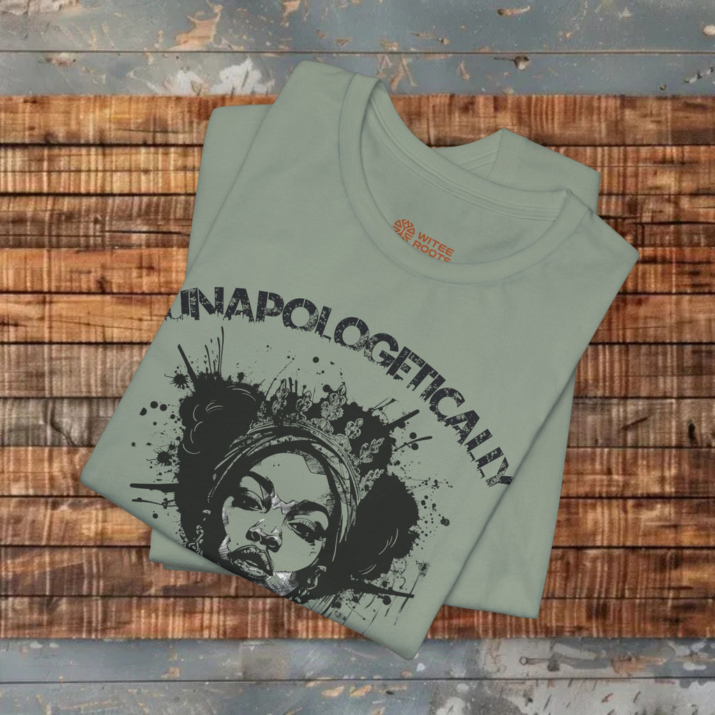A folded sage green t-shirt with a black graphic print of a woman's face and the word 'UNAPOLOGETICALLY' laid flat on a rustic wooden plank background.