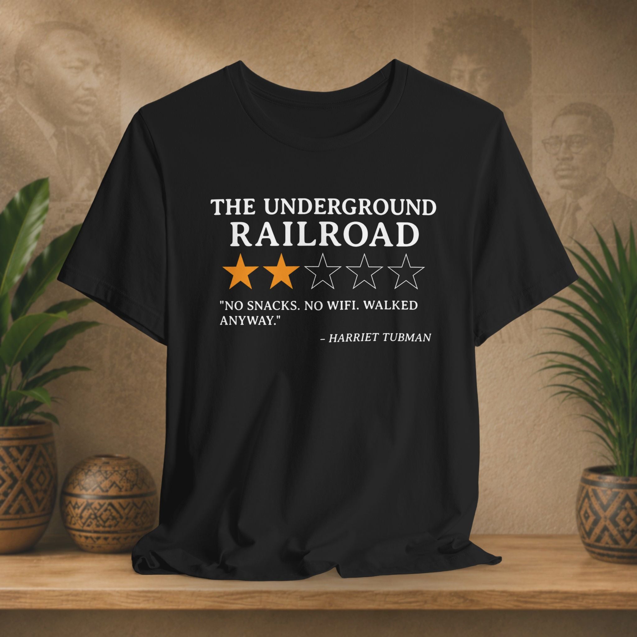 Black t-shirt with text and stars on a wooden surface with plants and wall art in the background