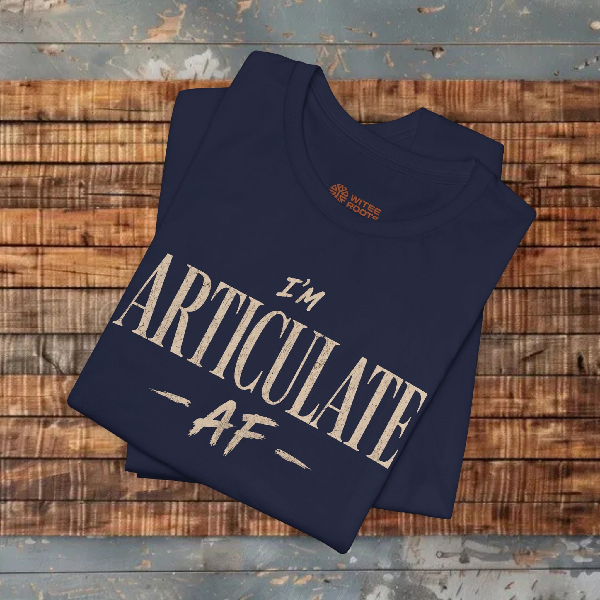 A navy crewneck t-shirt with the text 'I'M ARTICULATE AF' printed in a distressed beige font, displayed on a wooden background.