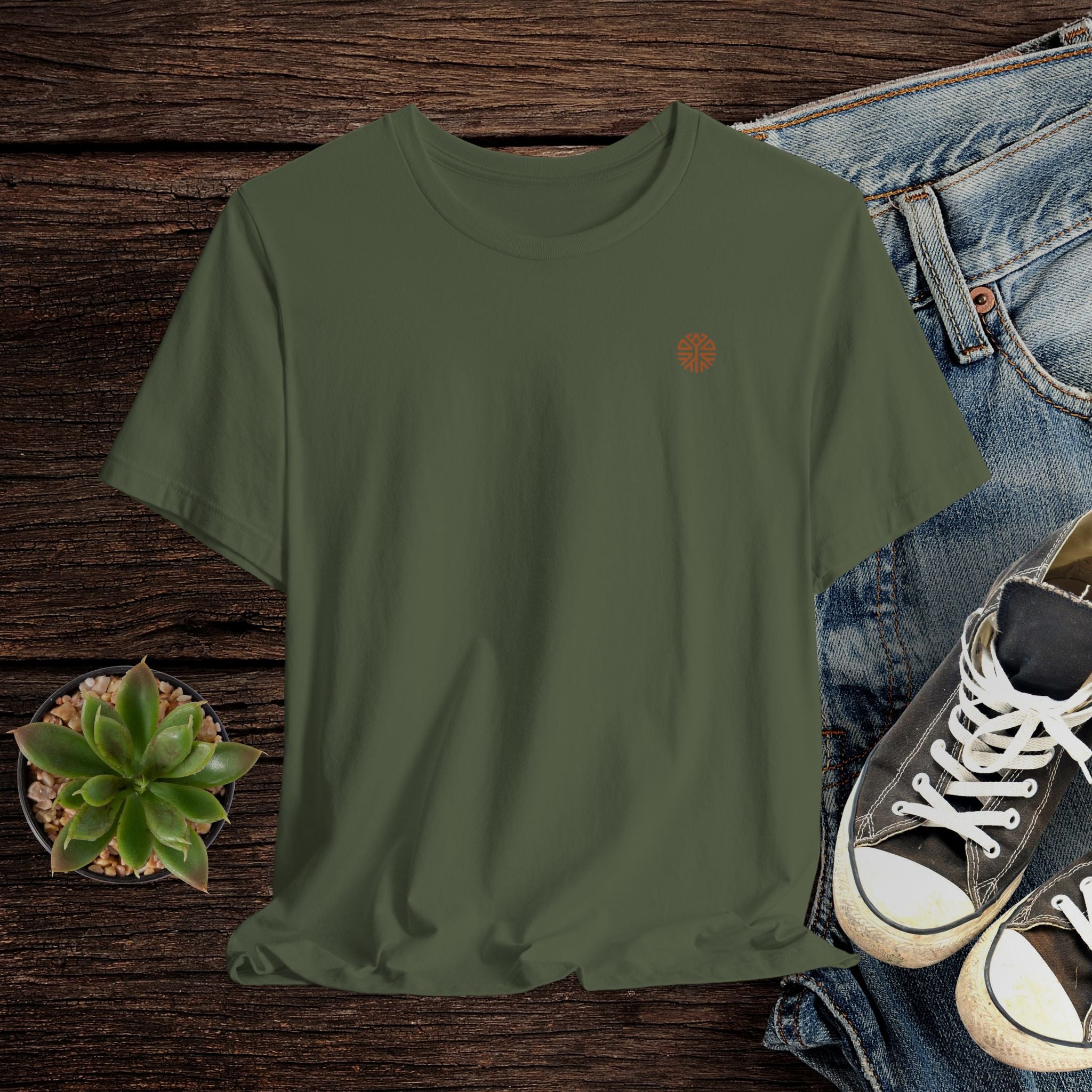 Green t-shirt with a small logo on a wooden surface with jeans and sneakers.