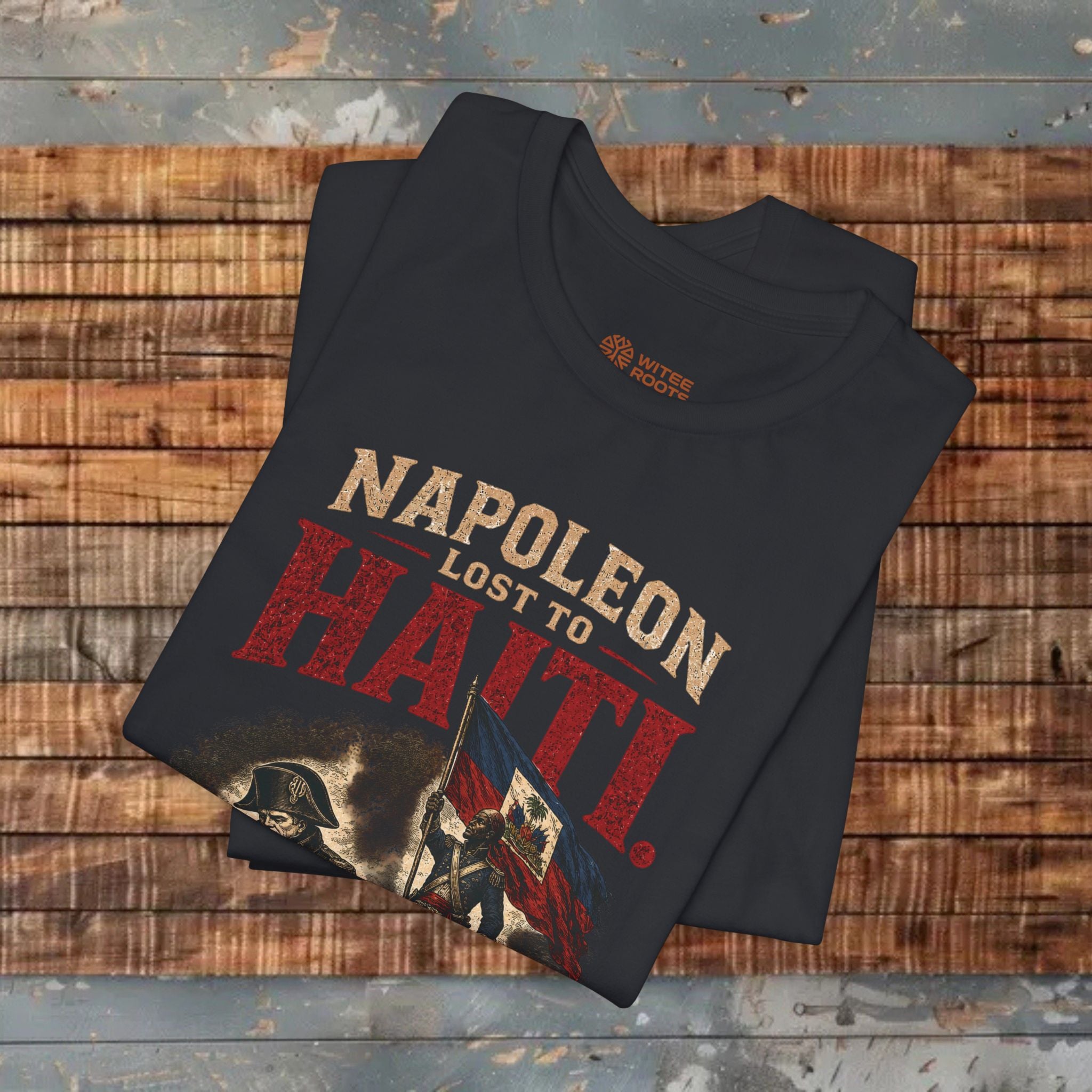 Folded black t-shirt with 'Napoleon Lost to Haiti' text on a wooden surface