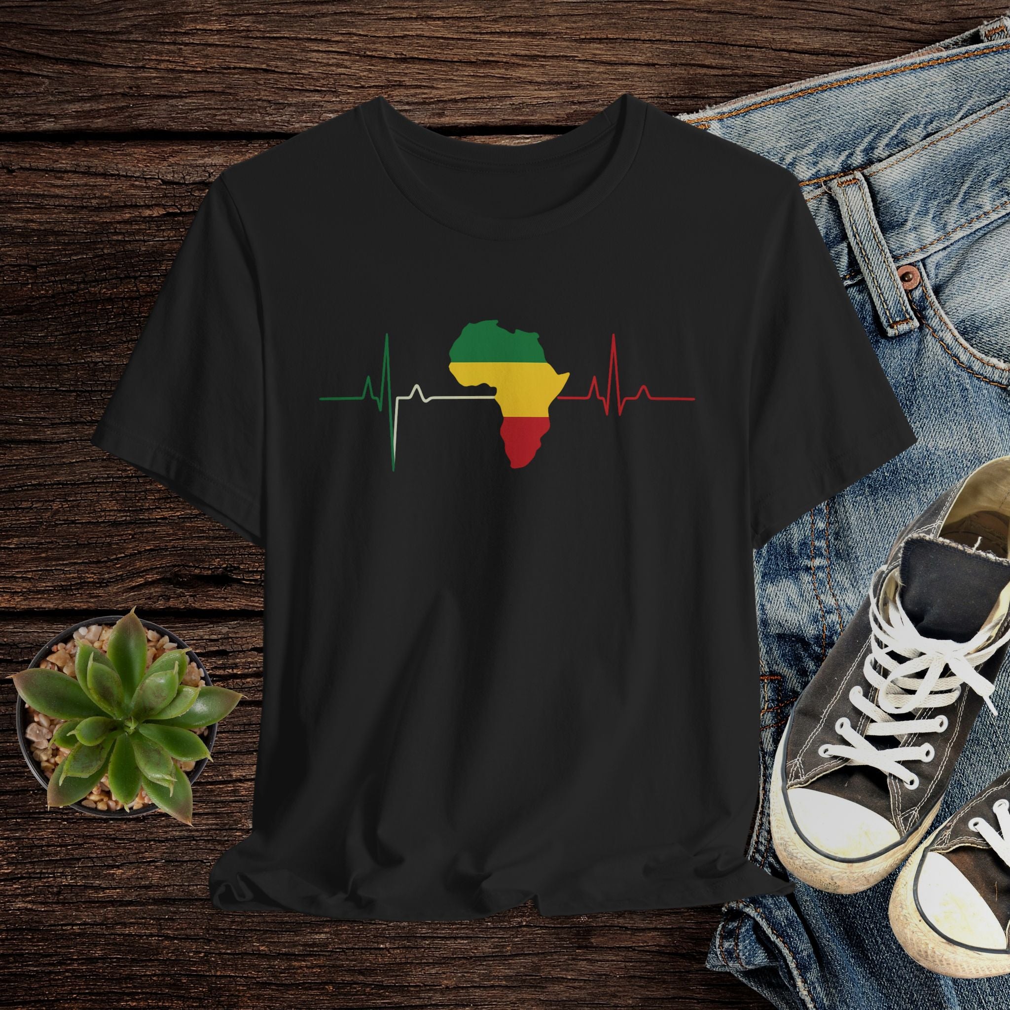 Black t-shirt with a colorful Africa map design on a wooden surface with jeans and sneakers.