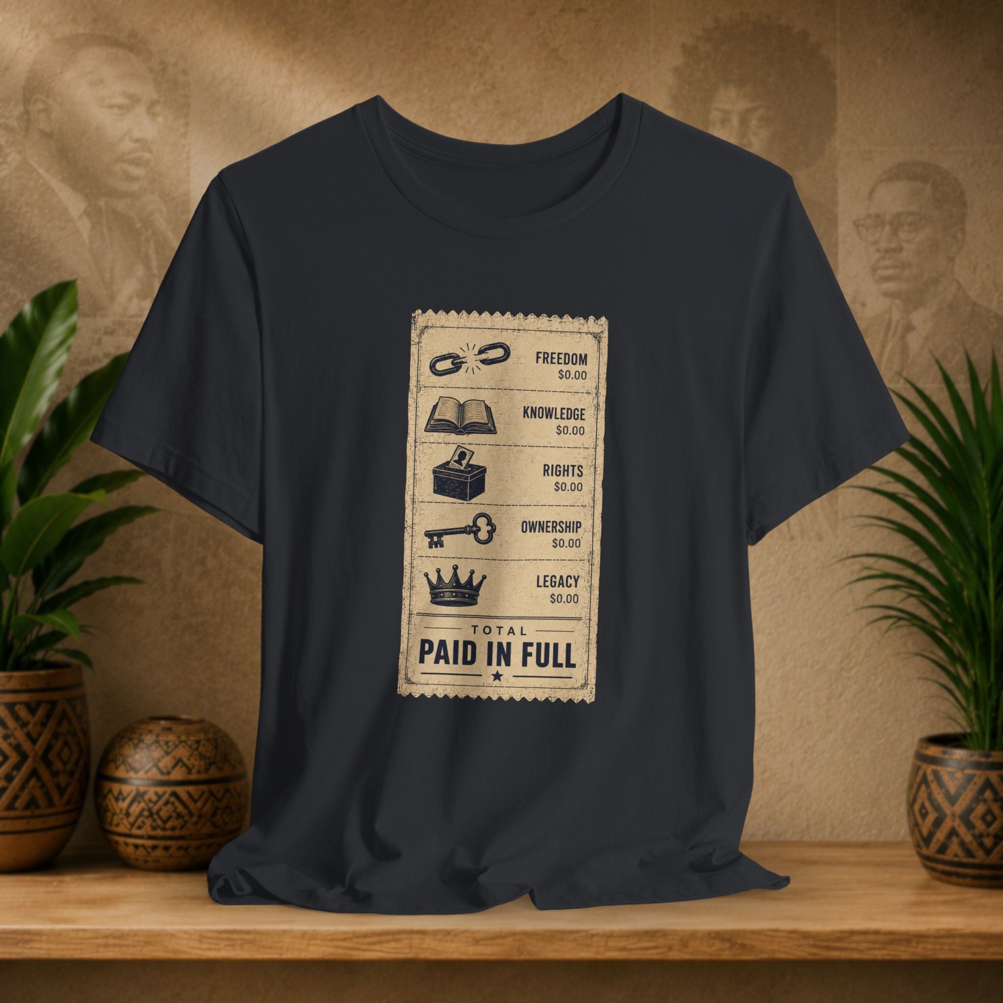 Black t-shirt with a graphic design on a wooden surface with plants and decorative items.