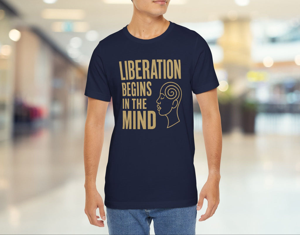 Man wearing a navy blue t-shirt with 'Liberation Begins in the Mind' text and graphic in a blurred indoor setting