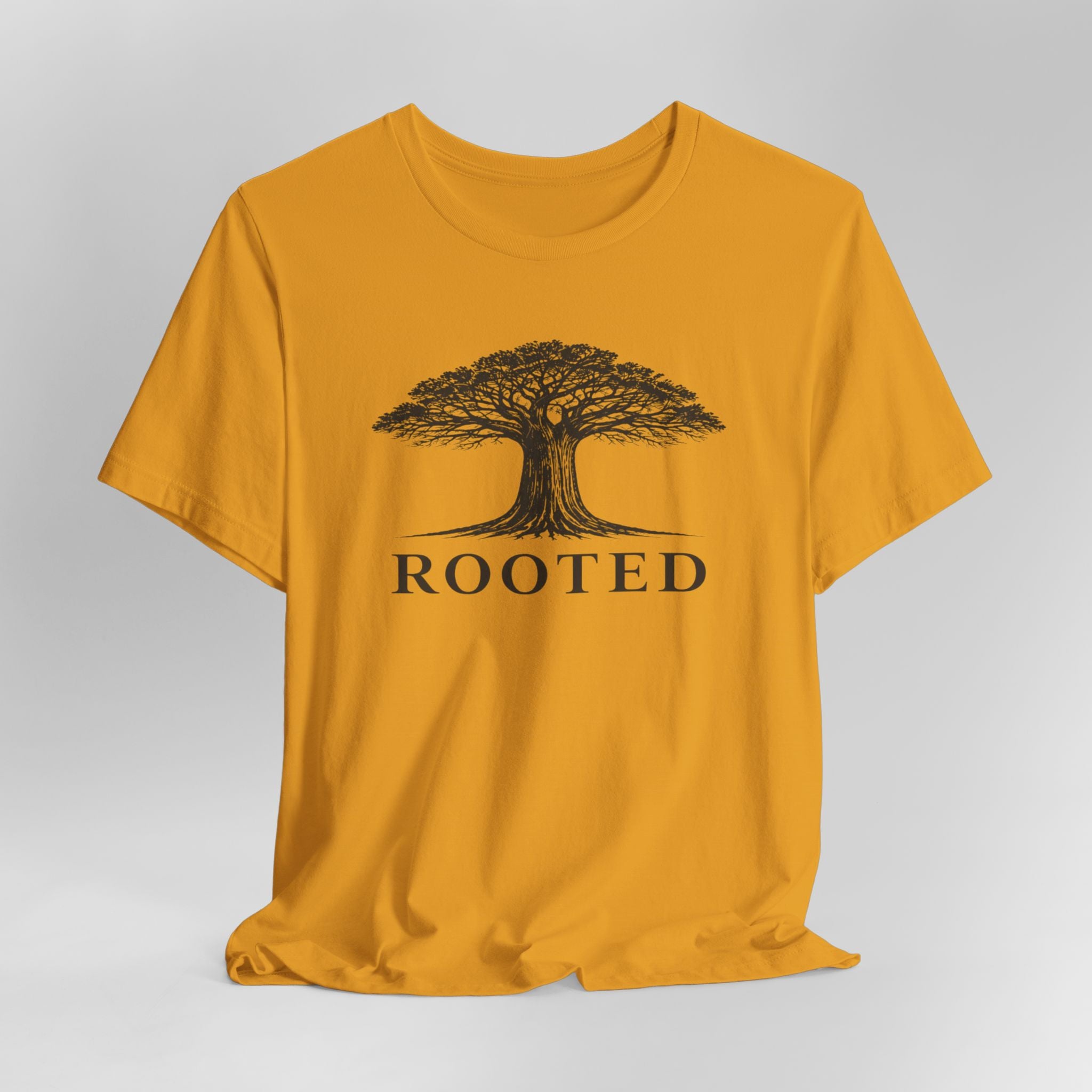 Mustard t-shirt with a tree graphic and 'ROOTED' text on a gray background
