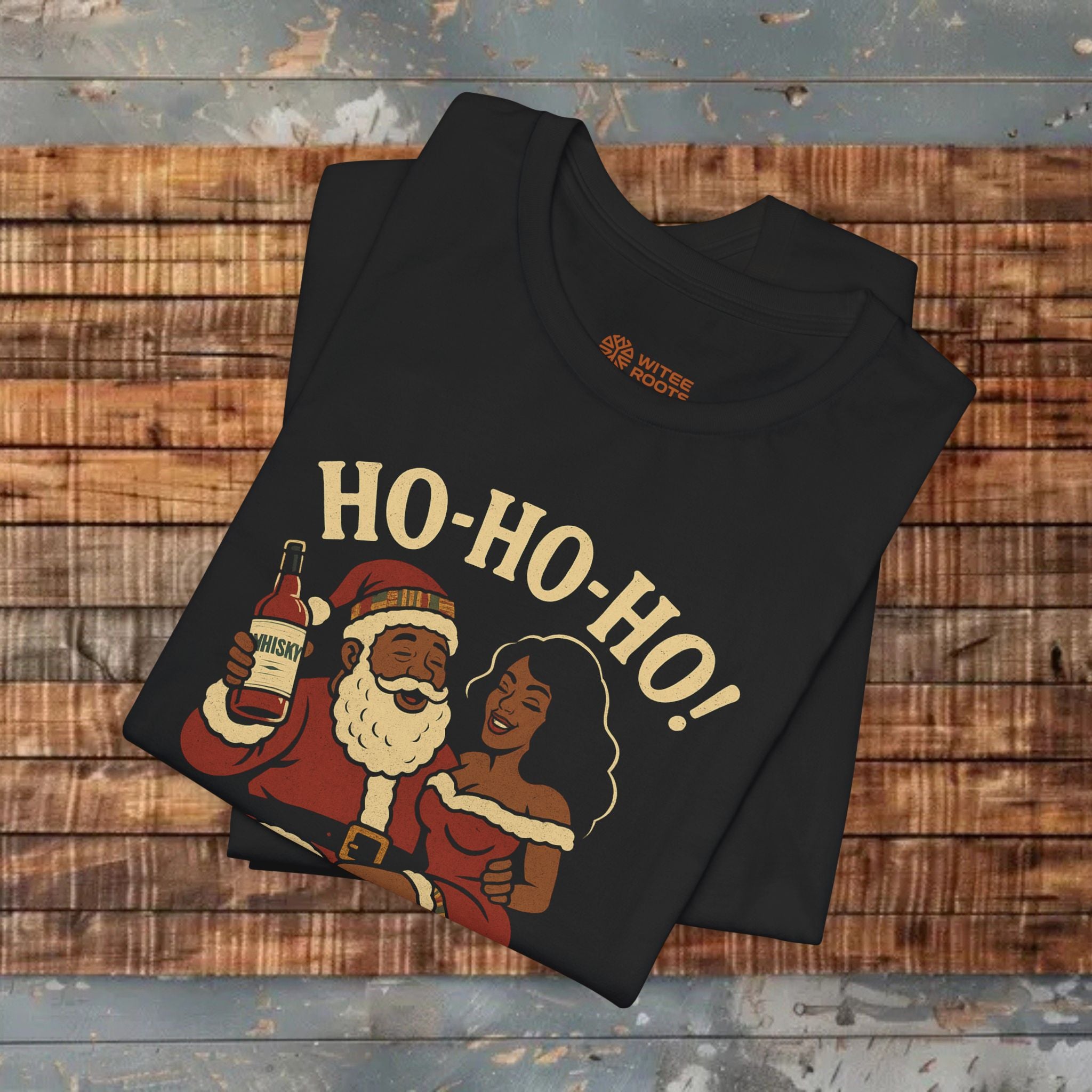 Black t-shirt with a graphic of Santa Claus and a woman, holding a bottle labeled 'Whiskey', with 'HO-HO-HO!' text on a wooden surface.