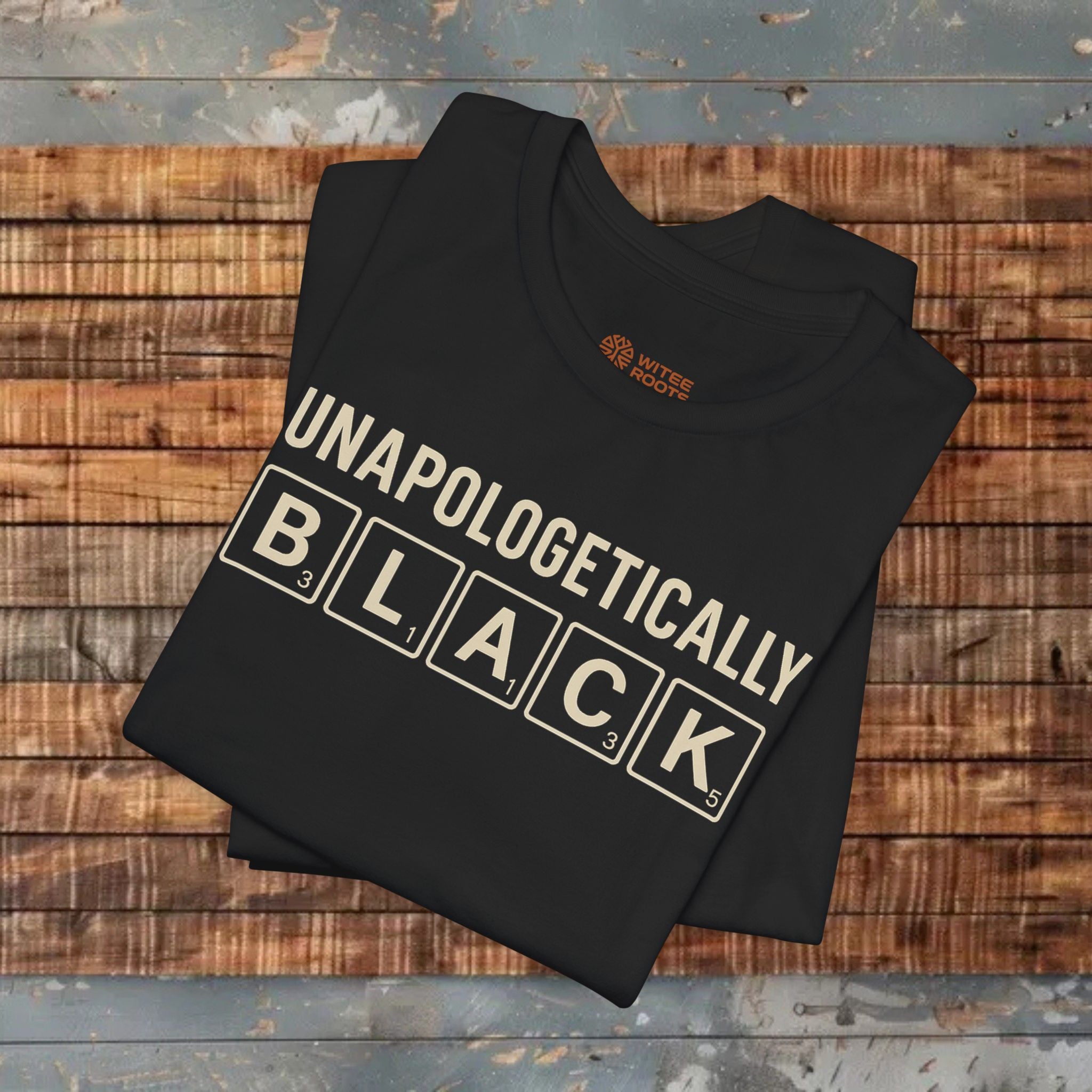 Folded black t-shirt with 'UNAPOLOGETICALLY BLACK' text on a wooden surface