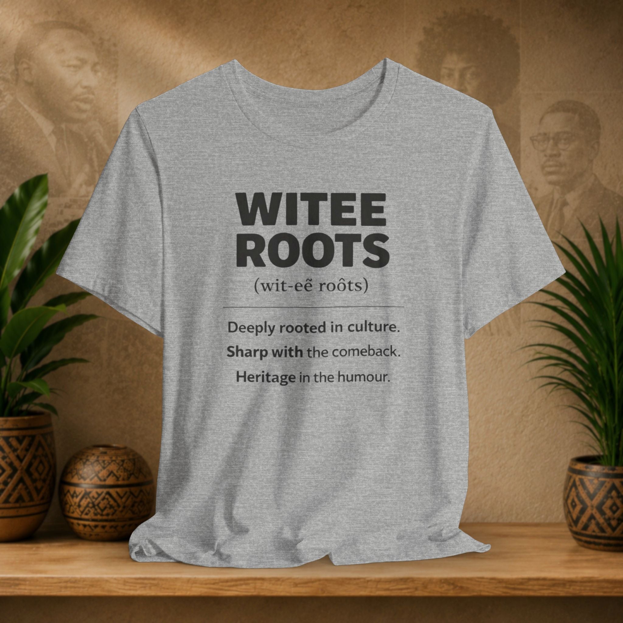 Gray t-shirt with 'WITEE ROOTS' text on a wooden surface with plants and a blurred background