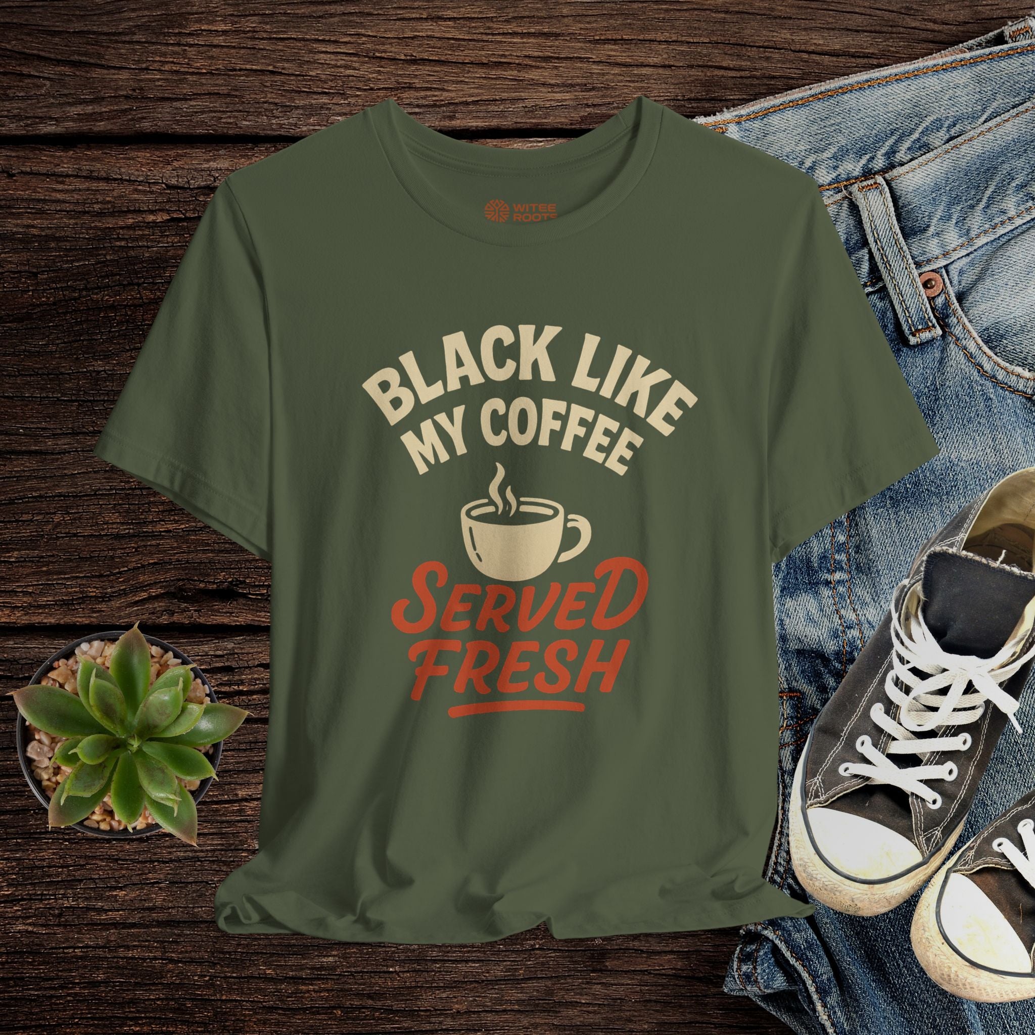 Green t-shirt with coffee-themed text on a wooden surface with jeans and shoes.