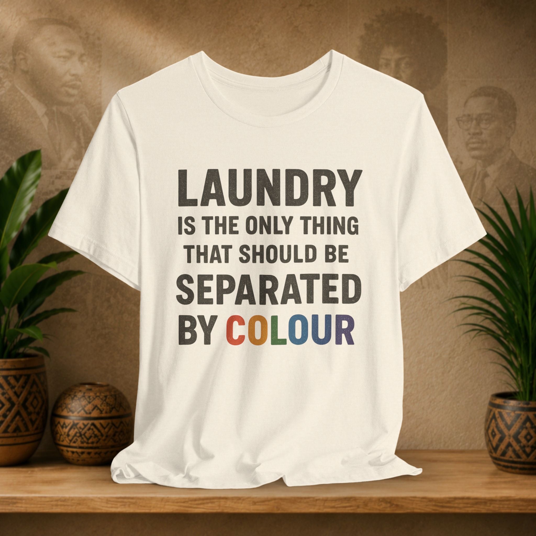 Beige t-shirt with humorous laundry text on a wooden surface with plants and a vintage-style portrait in the background.