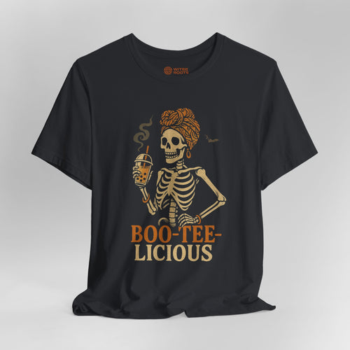 A black short-sleeve t-shirt with a graphic of a skeleton woman holding a beer, with the text 'BOO-TEE-LICIOUS' printed below in orange and beige. The shirt is displayed on a neutral gray background.