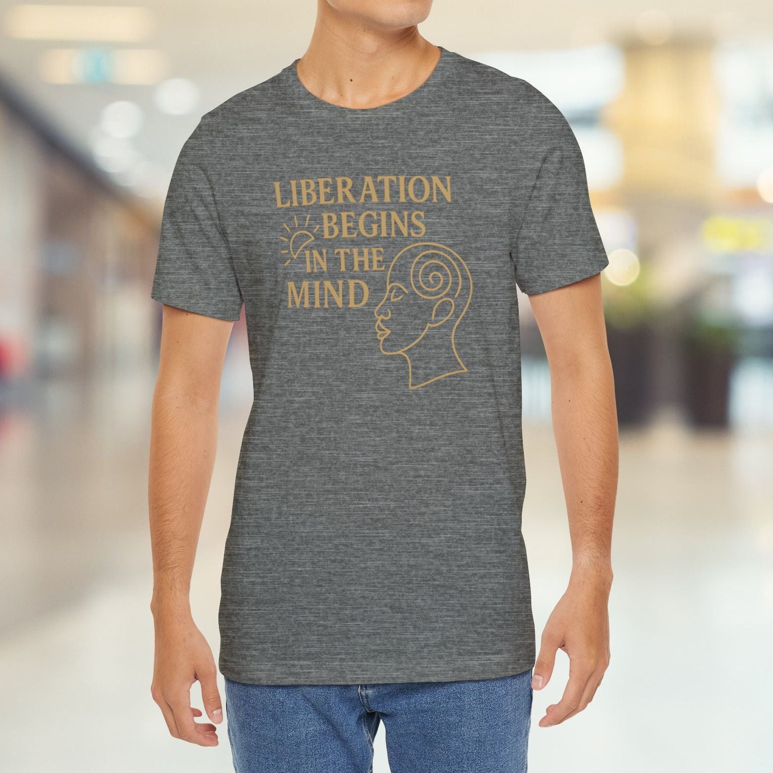 Man wearing a gray t-shirt with 'Liberation Begins in the Mind' text and graphic in a blurred indoor setting