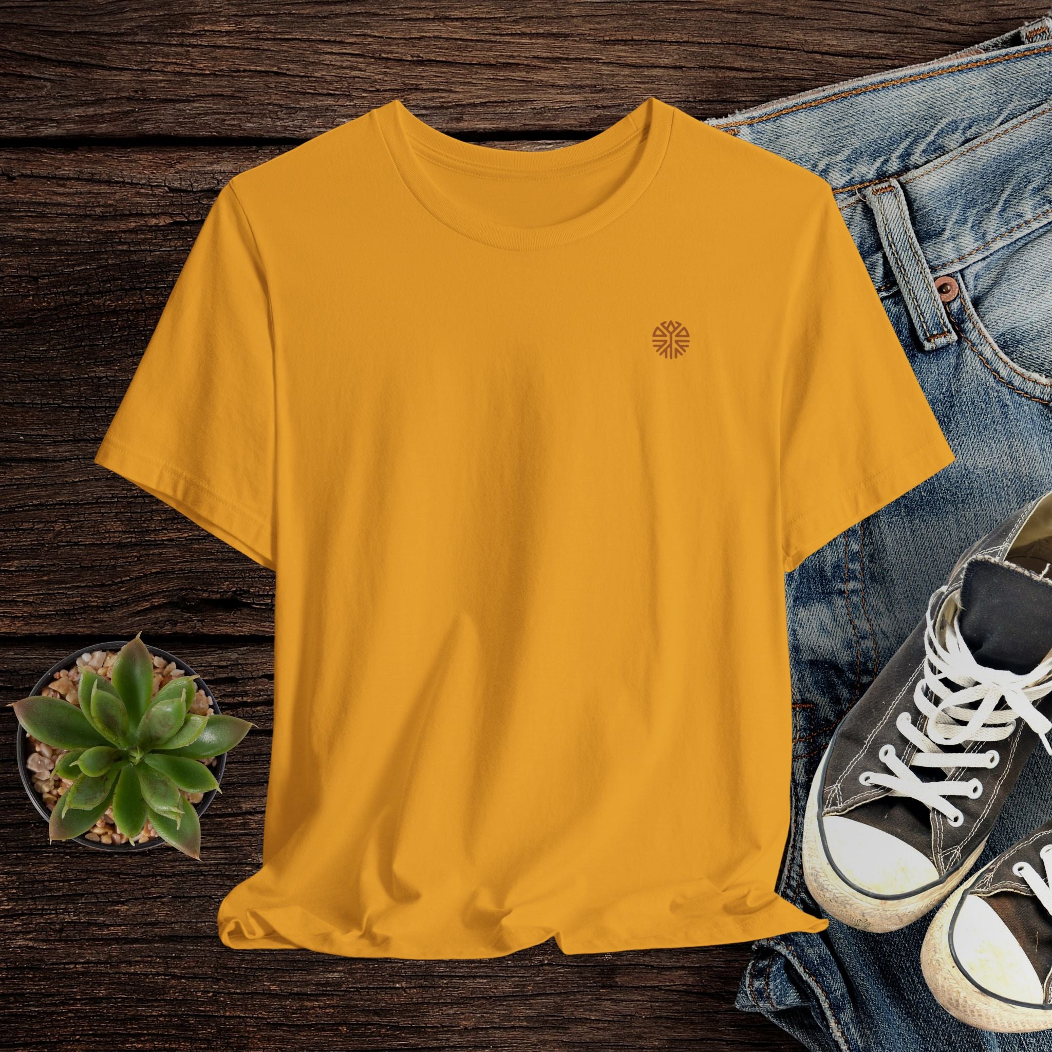 Mustard t-shirt with a logo on a wooden surface with jeans and sneakers.
