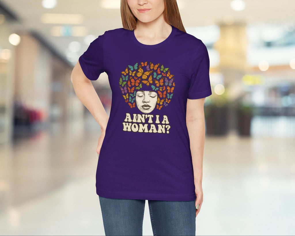 Person wearing a purple t-shirt with a colorful design and text in a blurred indoor setting