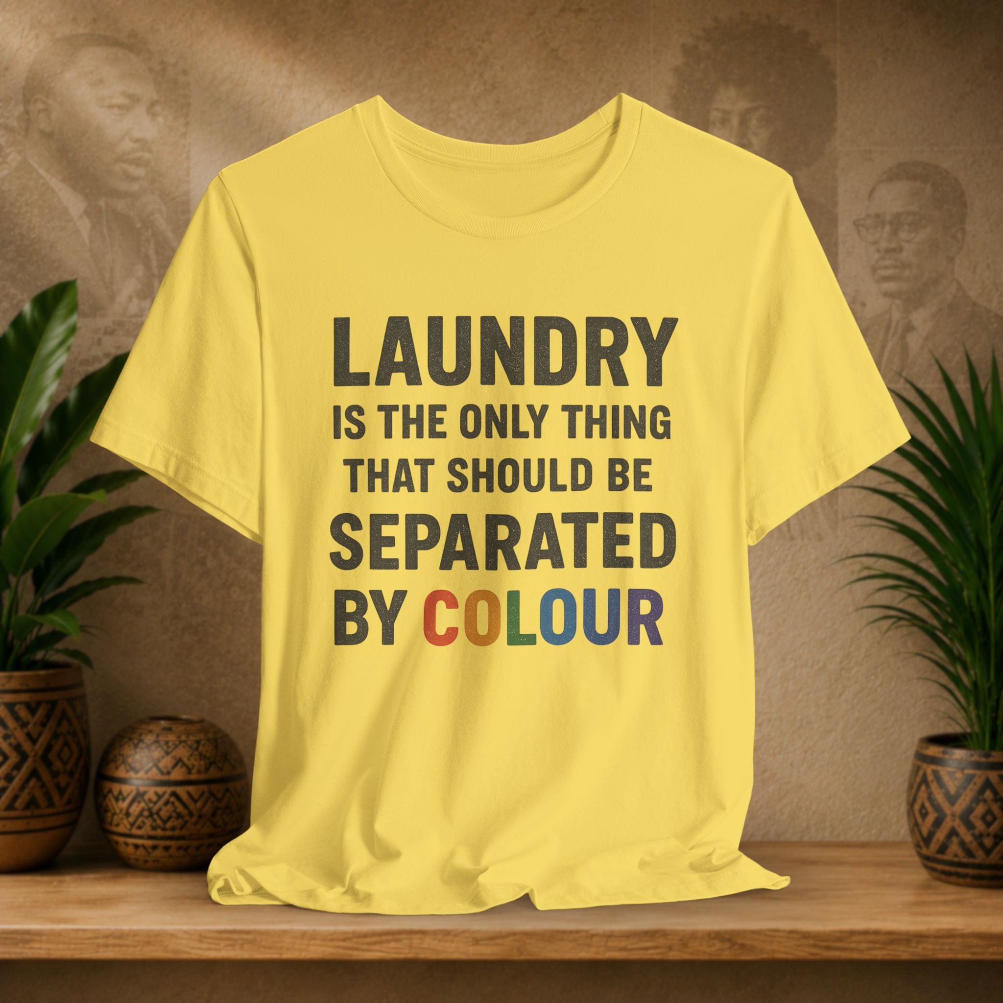 Yellow t-shirt with humorous laundry text on a wooden surface with plants and a vintage-style wall in the background.