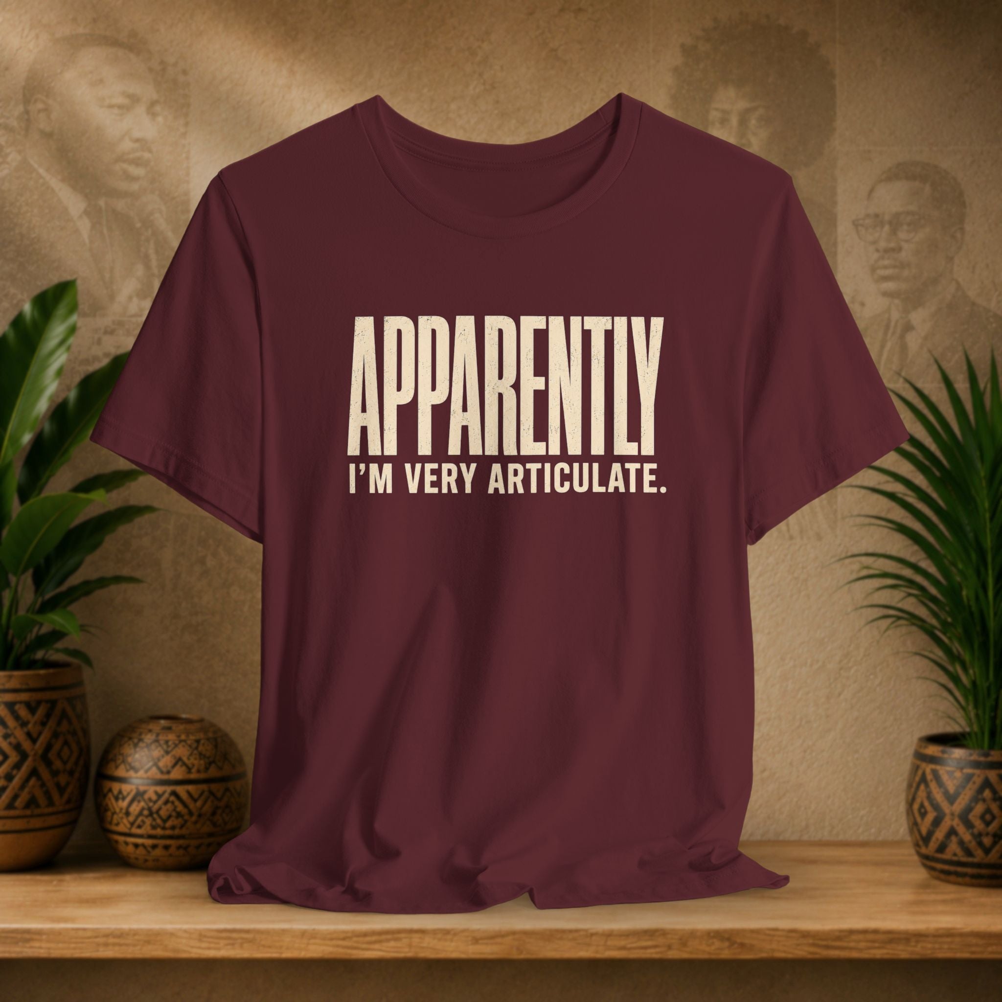 Maroon t-shirt with 'APPROPRIATELY I'M VERY ARTICULATE' text on a wooden surface with plants and wall art in the background.