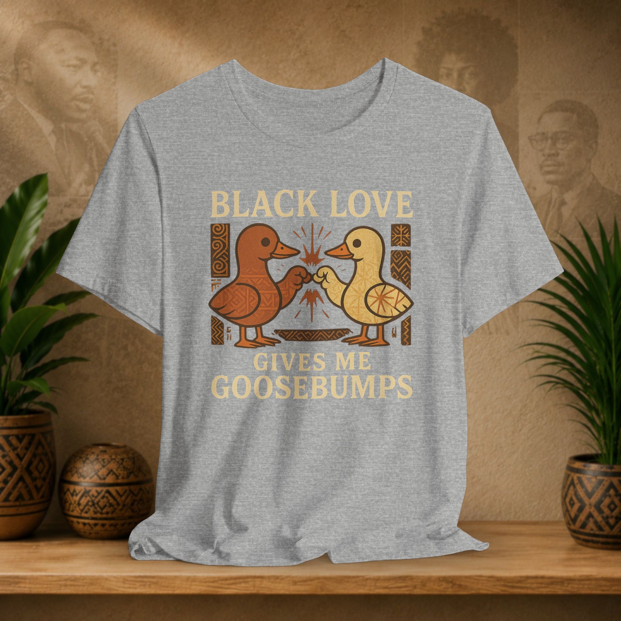 Gray t-shirt with 'Black Love Gives Me Goosebumps' graphic on a wooden shelf with plants and decorative items.