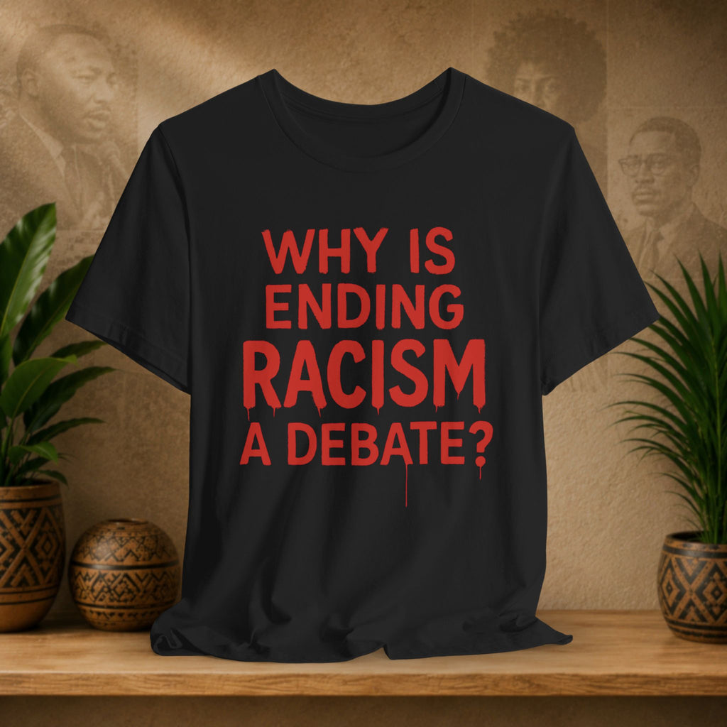 Black t-shirt with red text 'Why is ending racism a debate?' on a wooden surface with plants and a textured wall in the background.