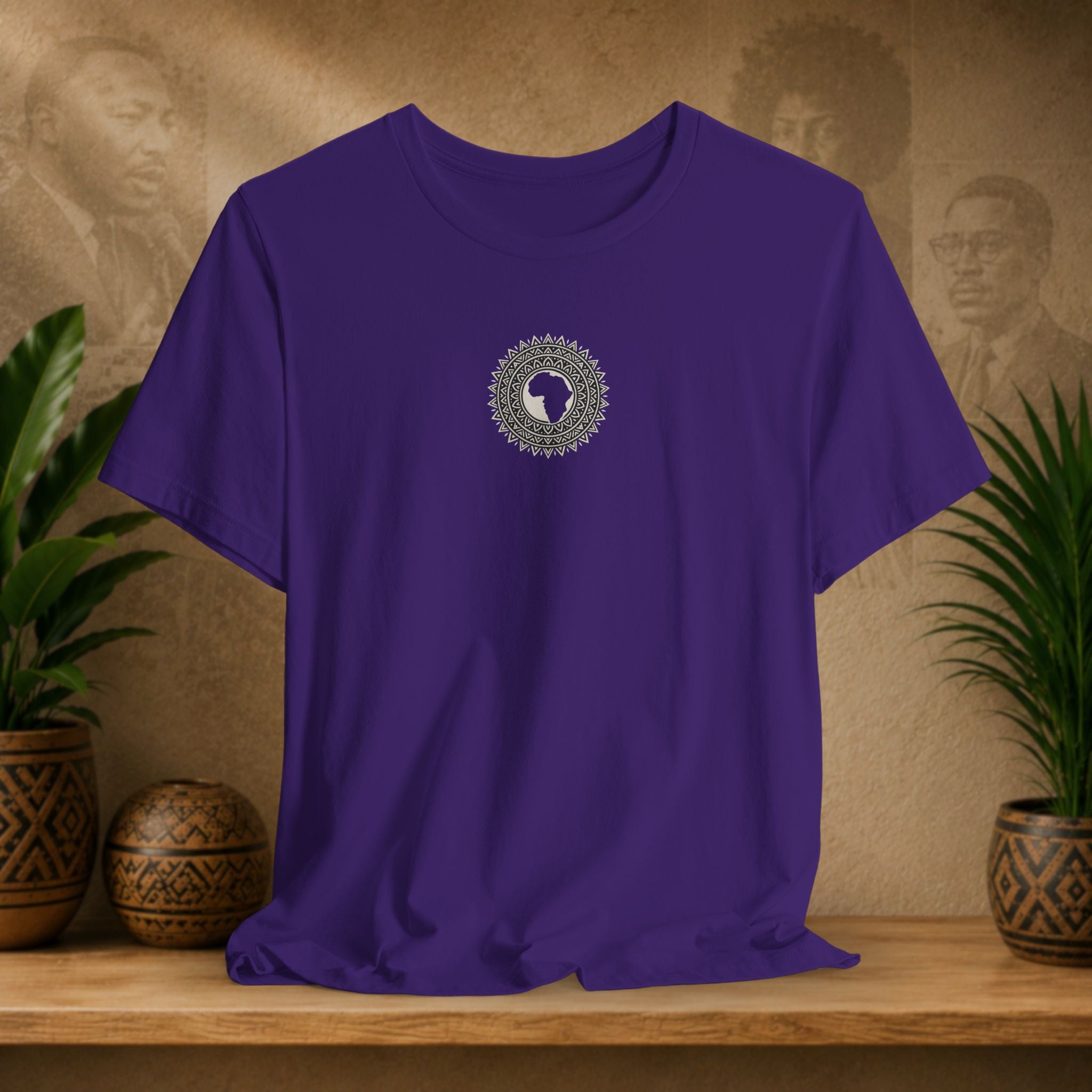 Purple t-shirt with a circular design on a wooden surface with plants and decorative items in the background.