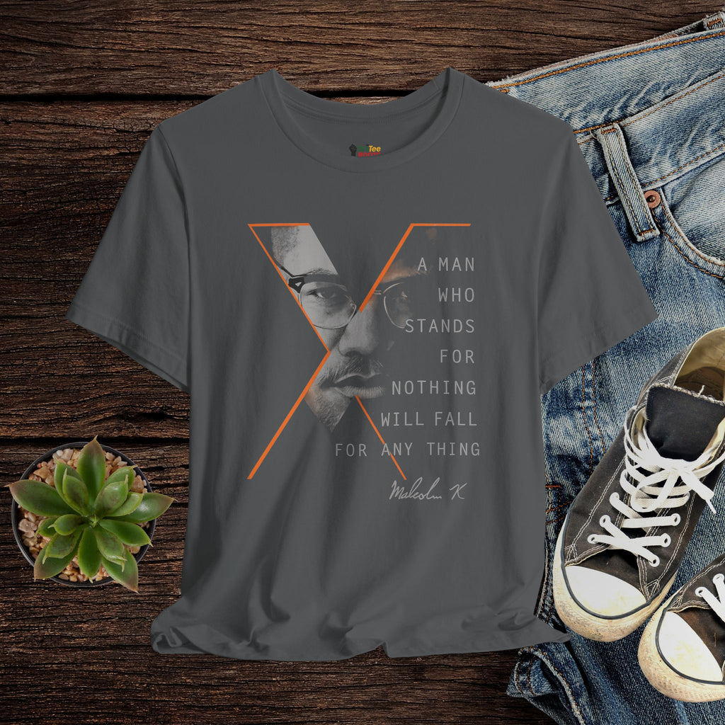 Gray t-shirt with graphic design and text, placed on a wooden surface with jeans and shoes.