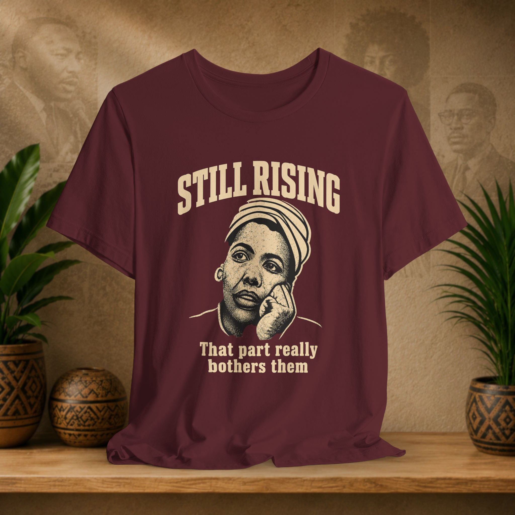 Maroon t-shirt with graphic and text on a wooden surface with plants and a textured wall background